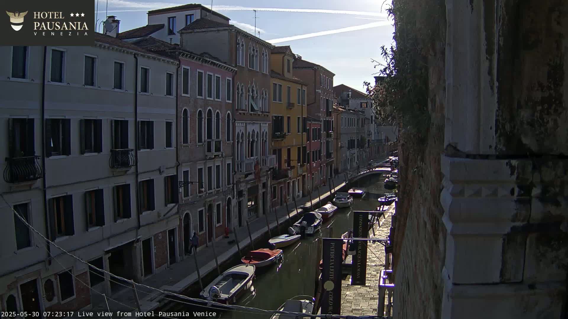 A sunny morning view down a Venetian canal, lined with closely spaced buildings, showing several boats moored along the waterway.