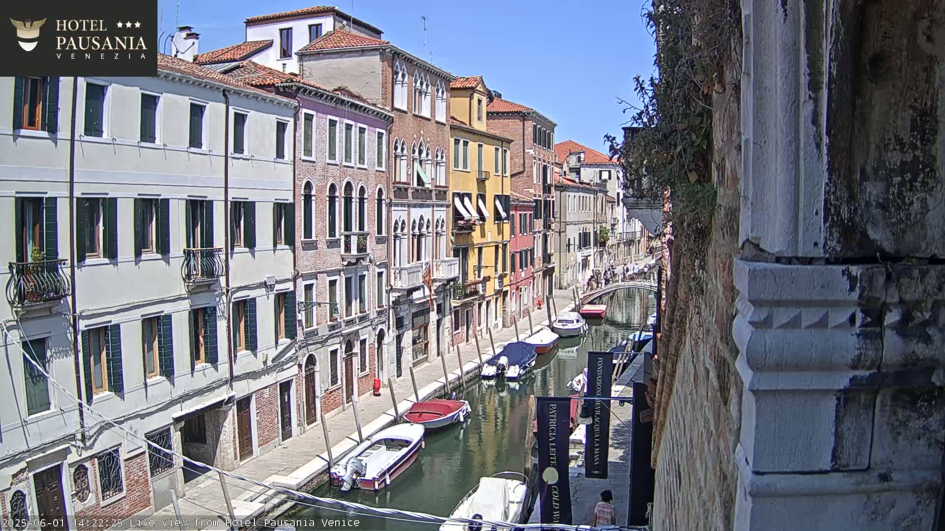 A sunny day in Venice shows a canal lined with colorful buildings and several boats moored along its banks.