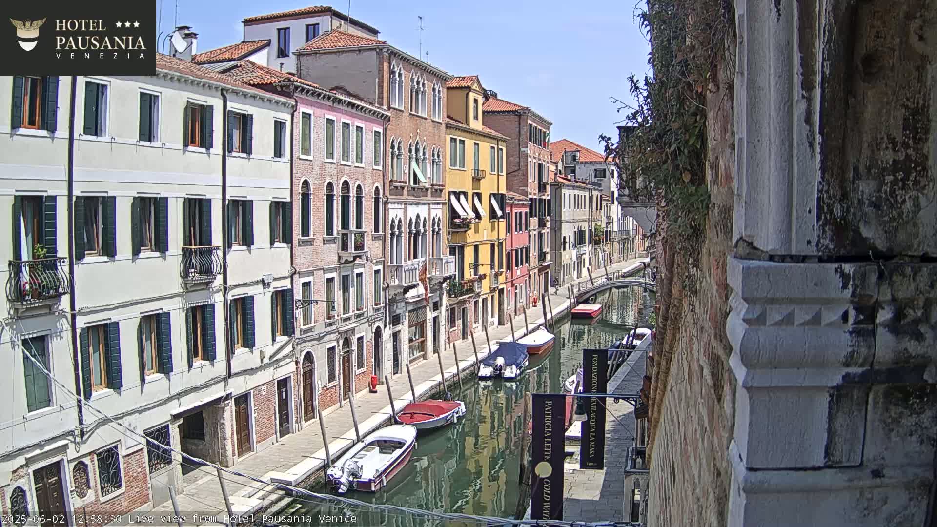 A sunny day in Venice shows a canal lined with colorful buildings, several small boats moored along the waterway.