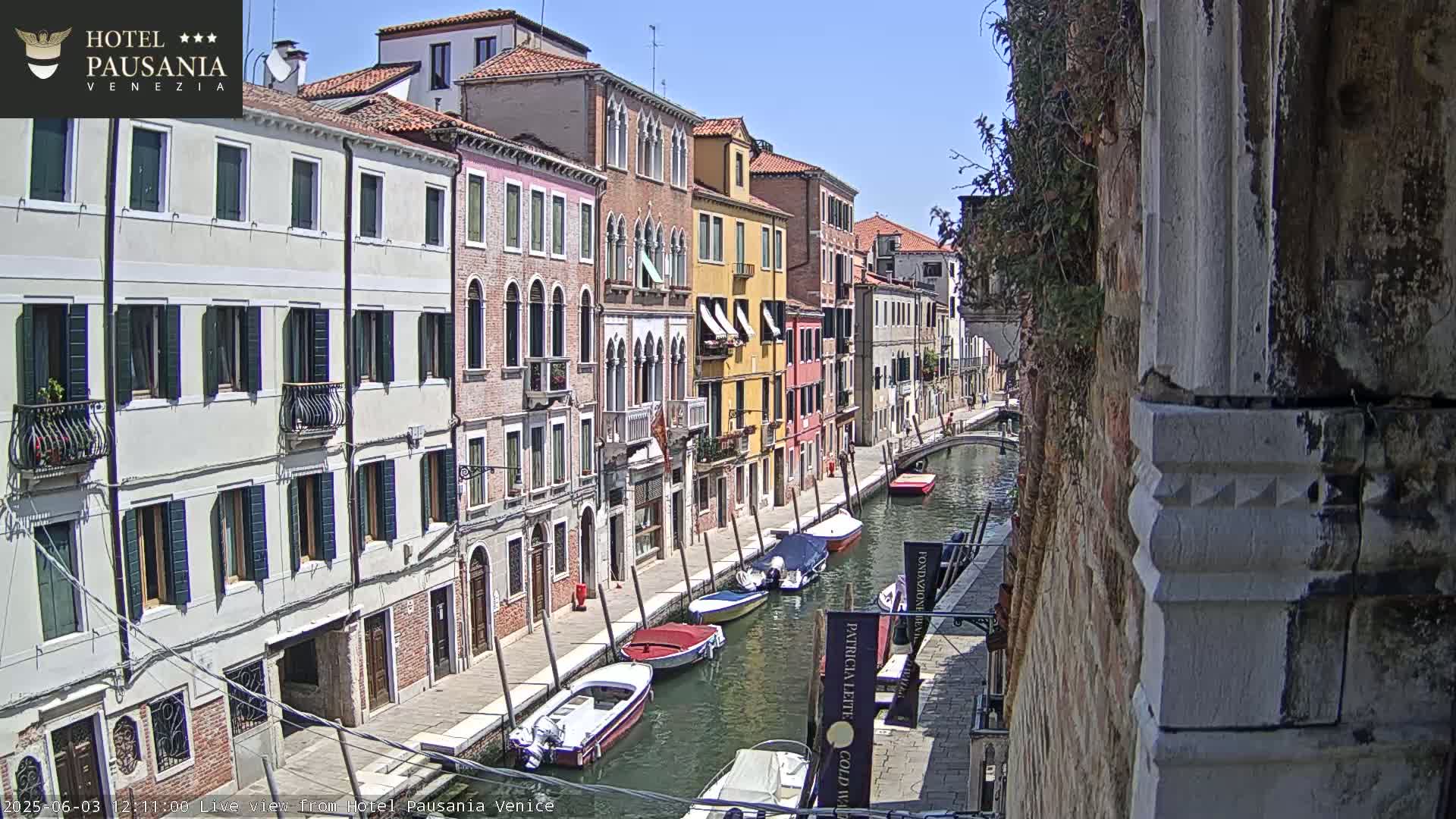 A sunny day in Venice shows colorful buildings lining a canal with several small motorboats moored along the waterway.