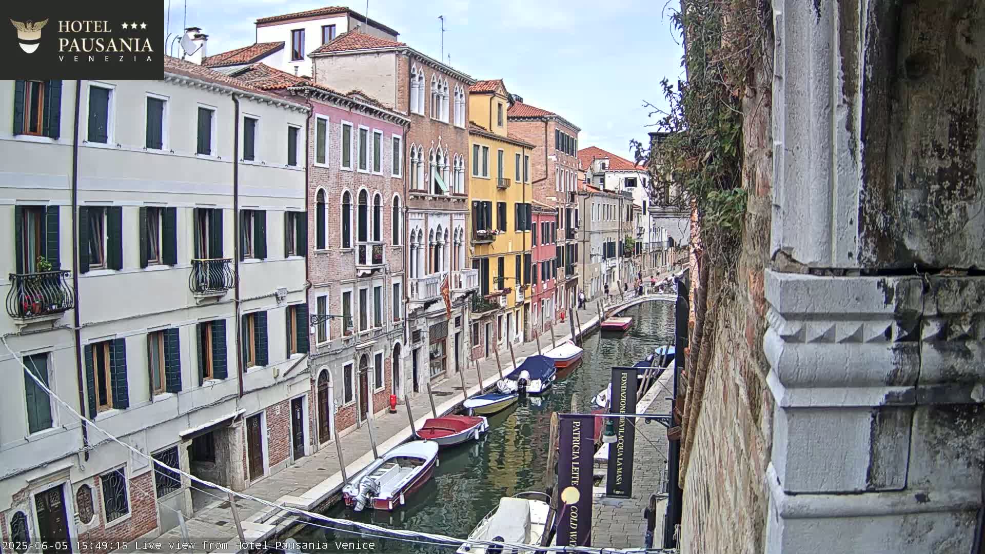 A canal in Venice, Italy, with several boats moored along its banks and colorful buildings lining the waterway under a partly cloudy sky.