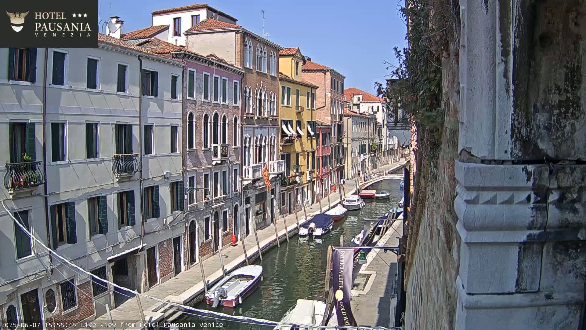 A sunny day in Venice shows a narrow canal lined with colorful buildings and several boats moored along its banks.
