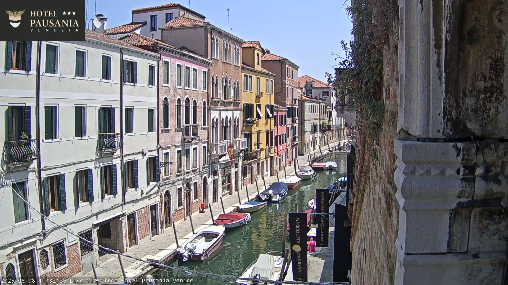 A sunny day in Venice shows a narrow canal lined with colorful buildings and several moored boats.