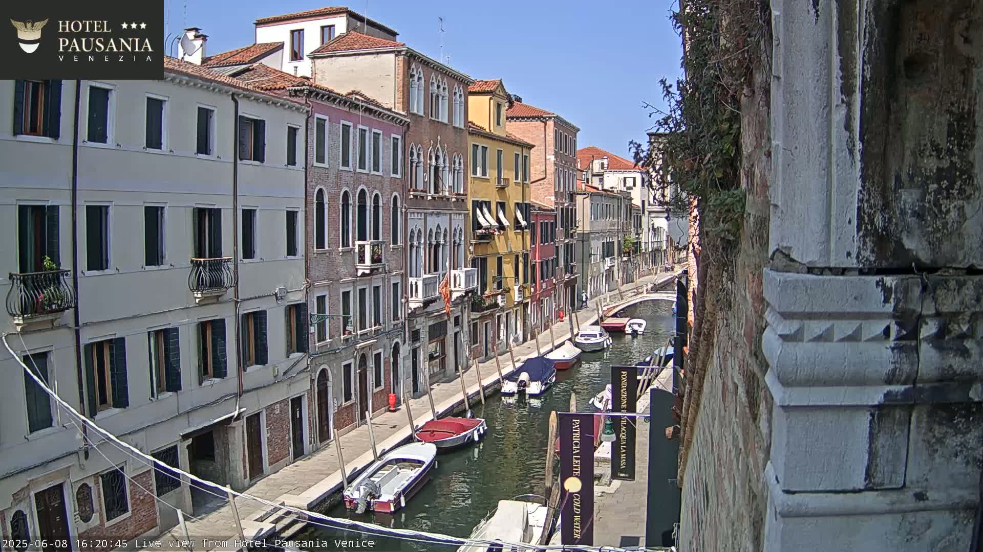 A sunny day in Venice shows a canal lined with colorful buildings and several small boats moored along the waterway.