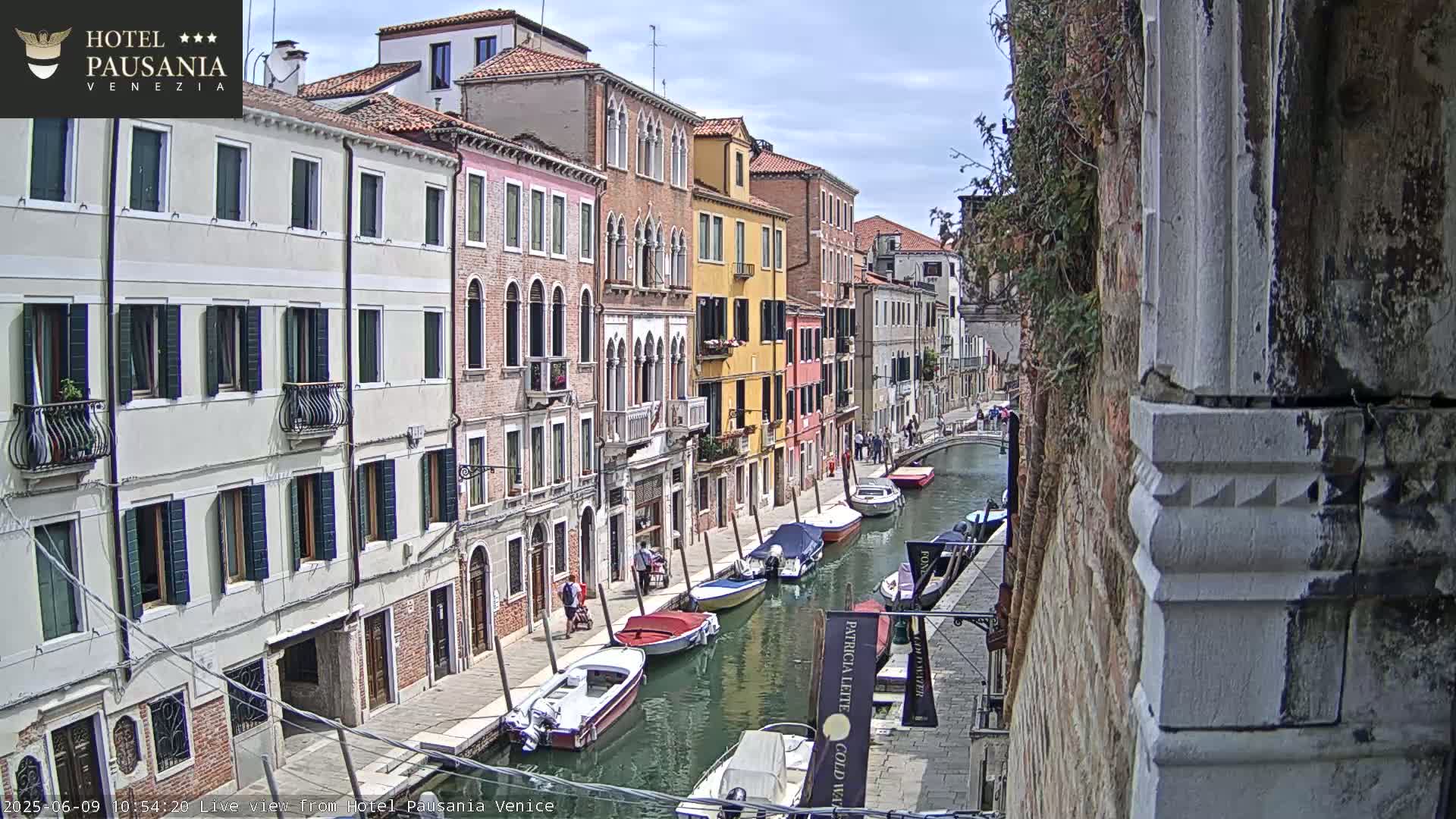 A sunny day in Venice shows a canal lined with colorful buildings and several moored boats.