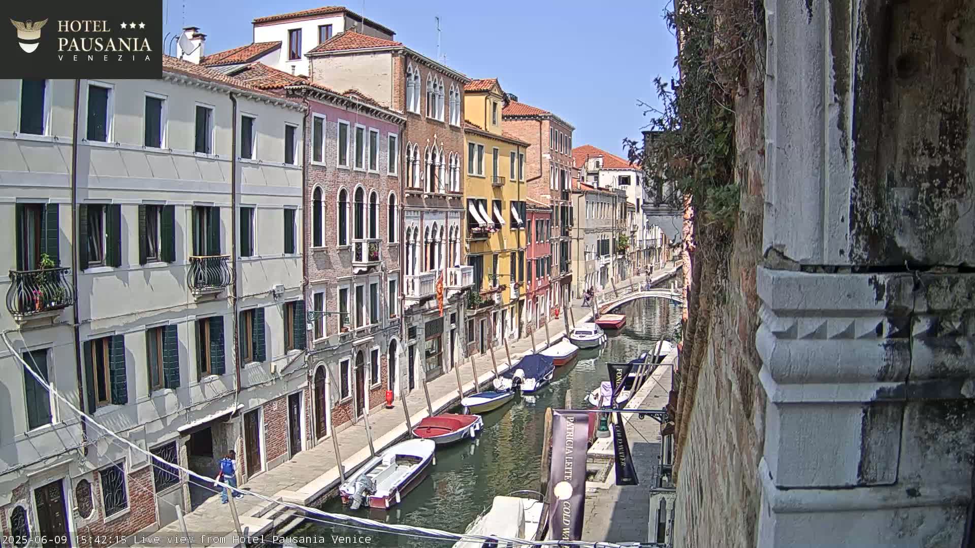 A sunny day in Venice shows several boats moored along a canal beside colorful buildings.