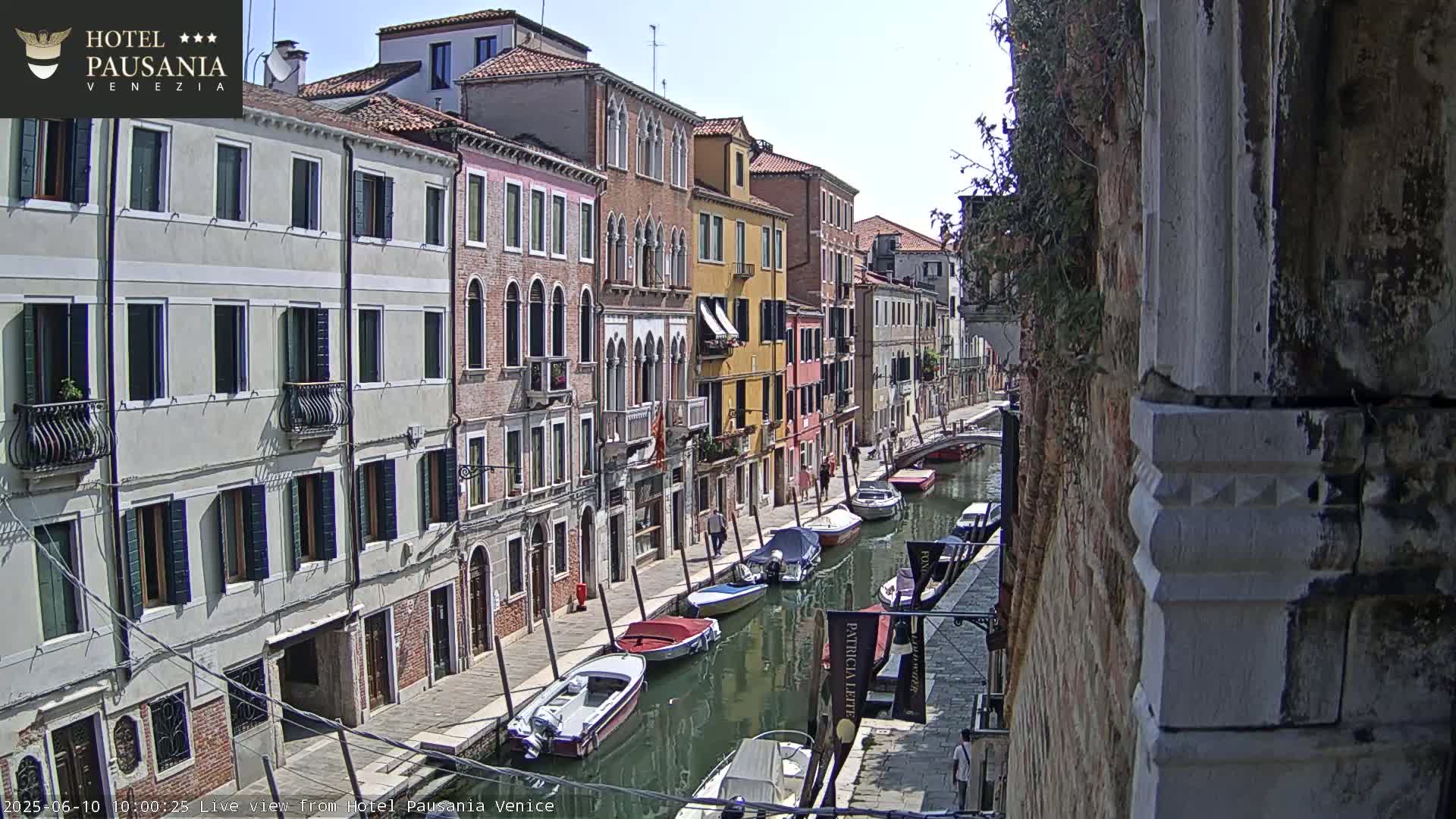 A sunny day in Venice shows a narrow canal lined with colorful buildings and several moored boats.
