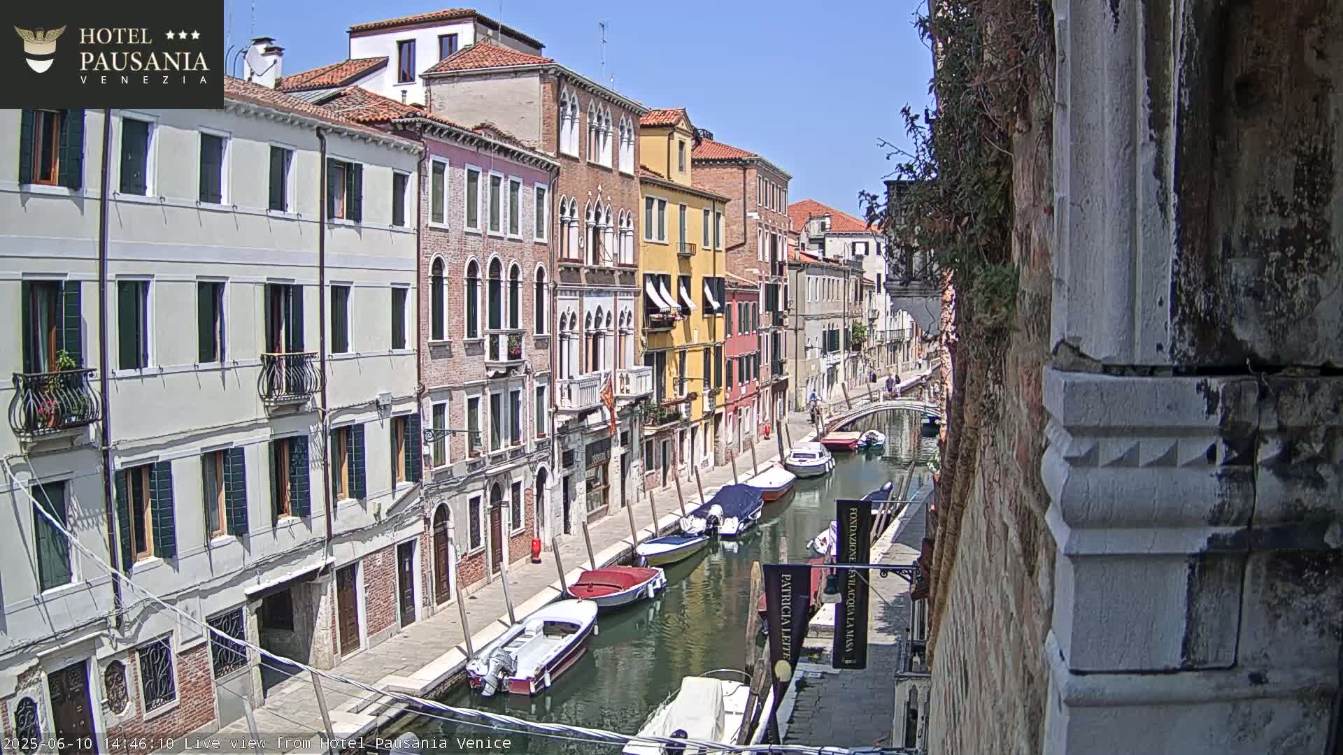 A sunny Venetian canal is lined with colorful buildings and several moored boats.