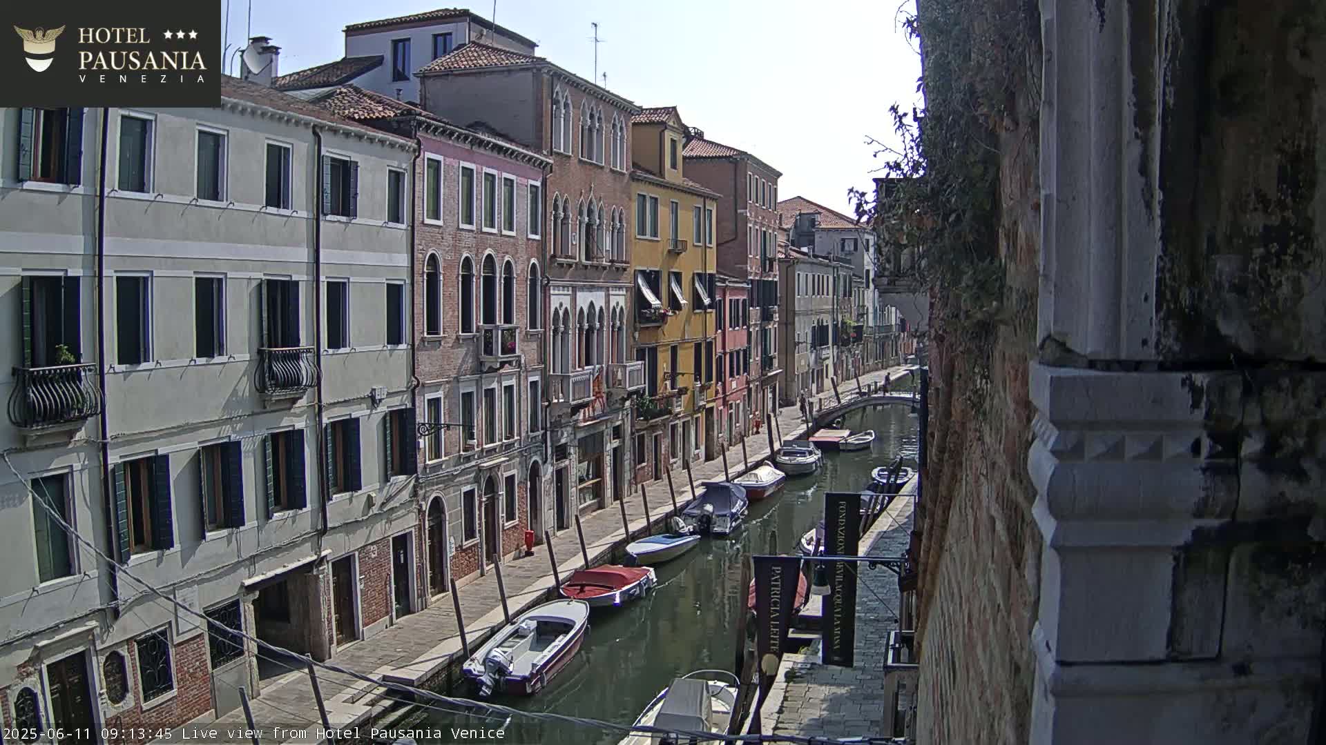 A sunny day in Venice shows several colorful buildings lining a canal where numerous small boats are moored.