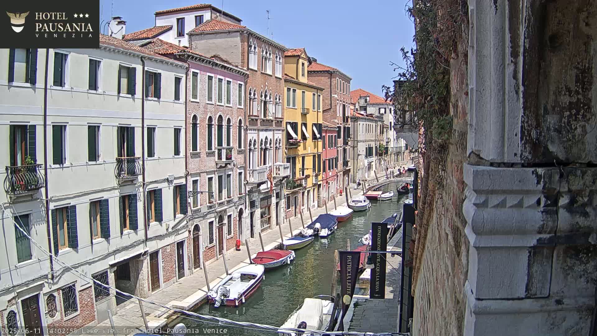 A sunny day in Venice shows colorful buildings lining a canal filled with several moored boats.