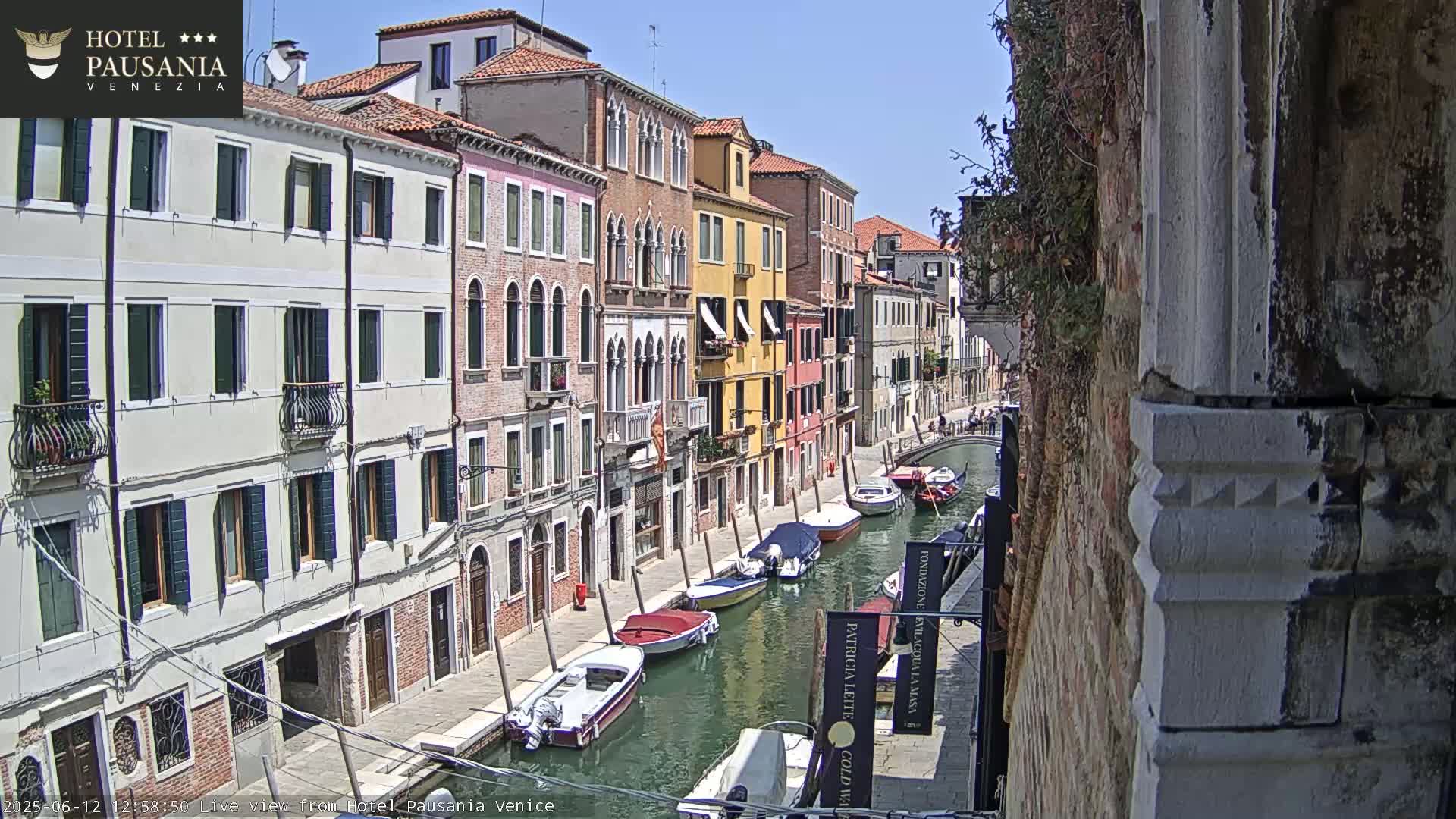 A sunny day in Venice shows a narrow canal lined with colorful buildings and several motorboats and gondolas.