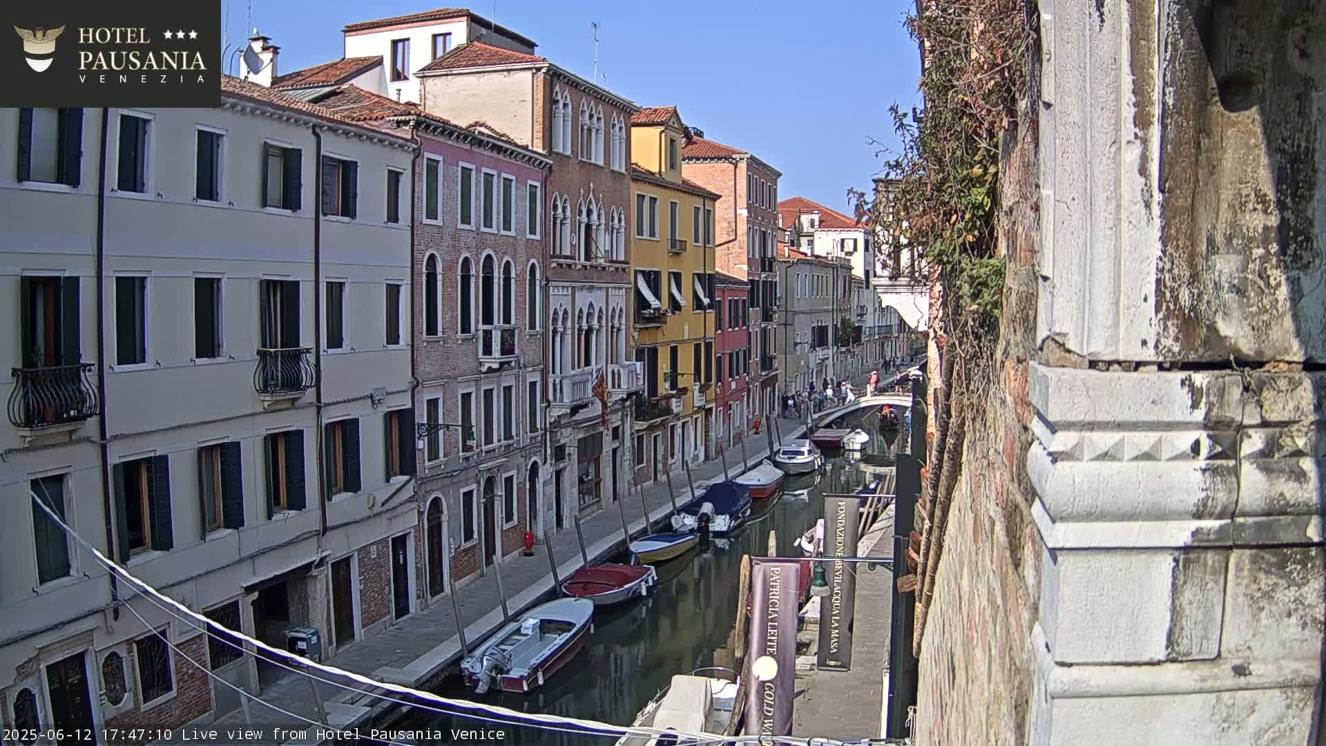 A sunny view down a Venetian canal, lined with colorful buildings and several moored boats.