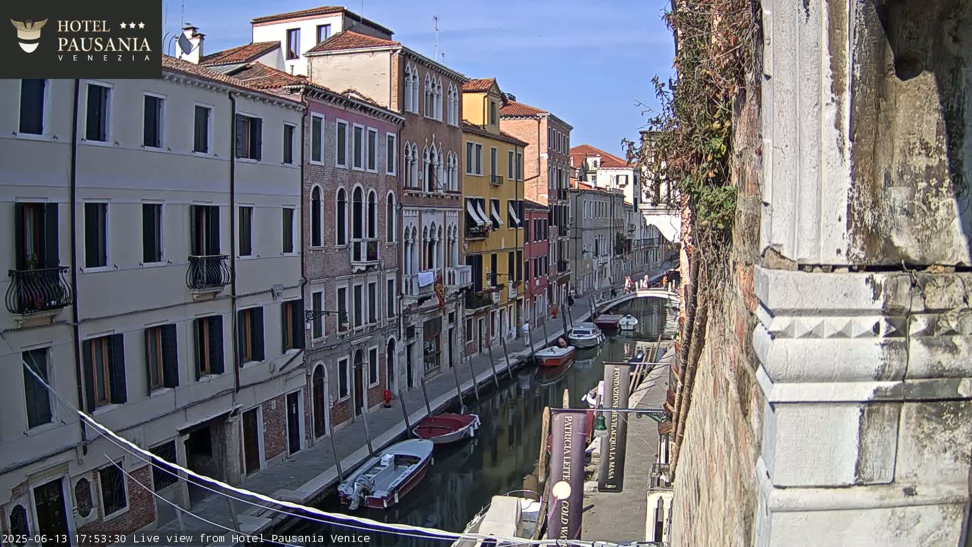 A sunny day in Venice shows colorful buildings lining a canal with several boats moored along its edge.