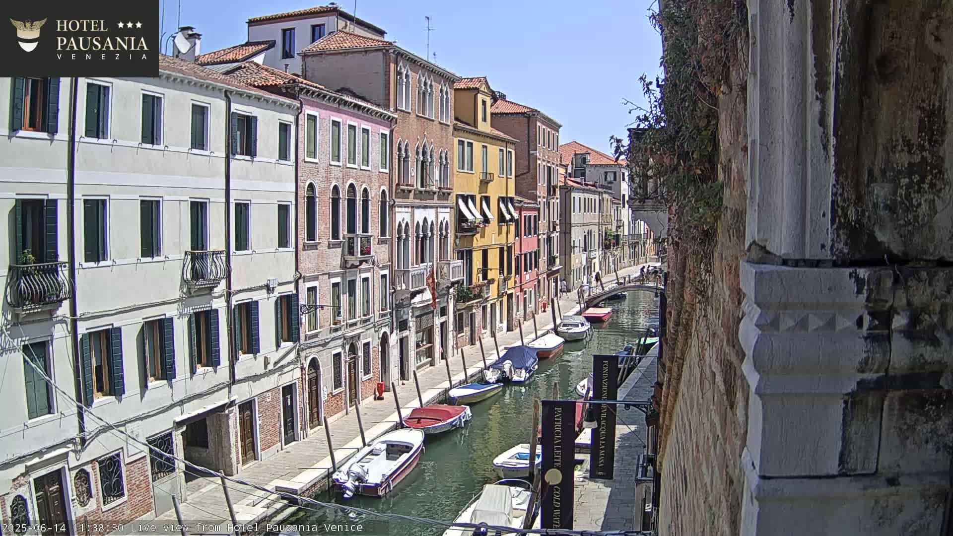 A sunny day in Venice shows a canal lined with colorful buildings and several moored boats.