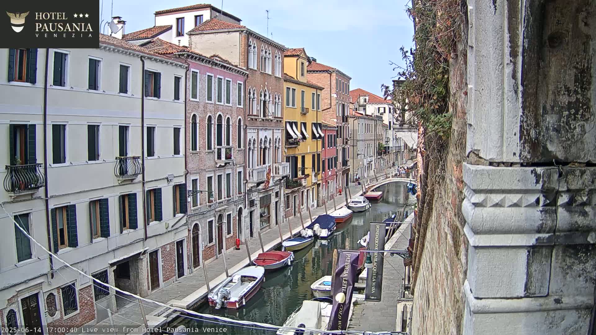 A sunny view down a Venetian canal lined with colorful buildings and several moored boats.