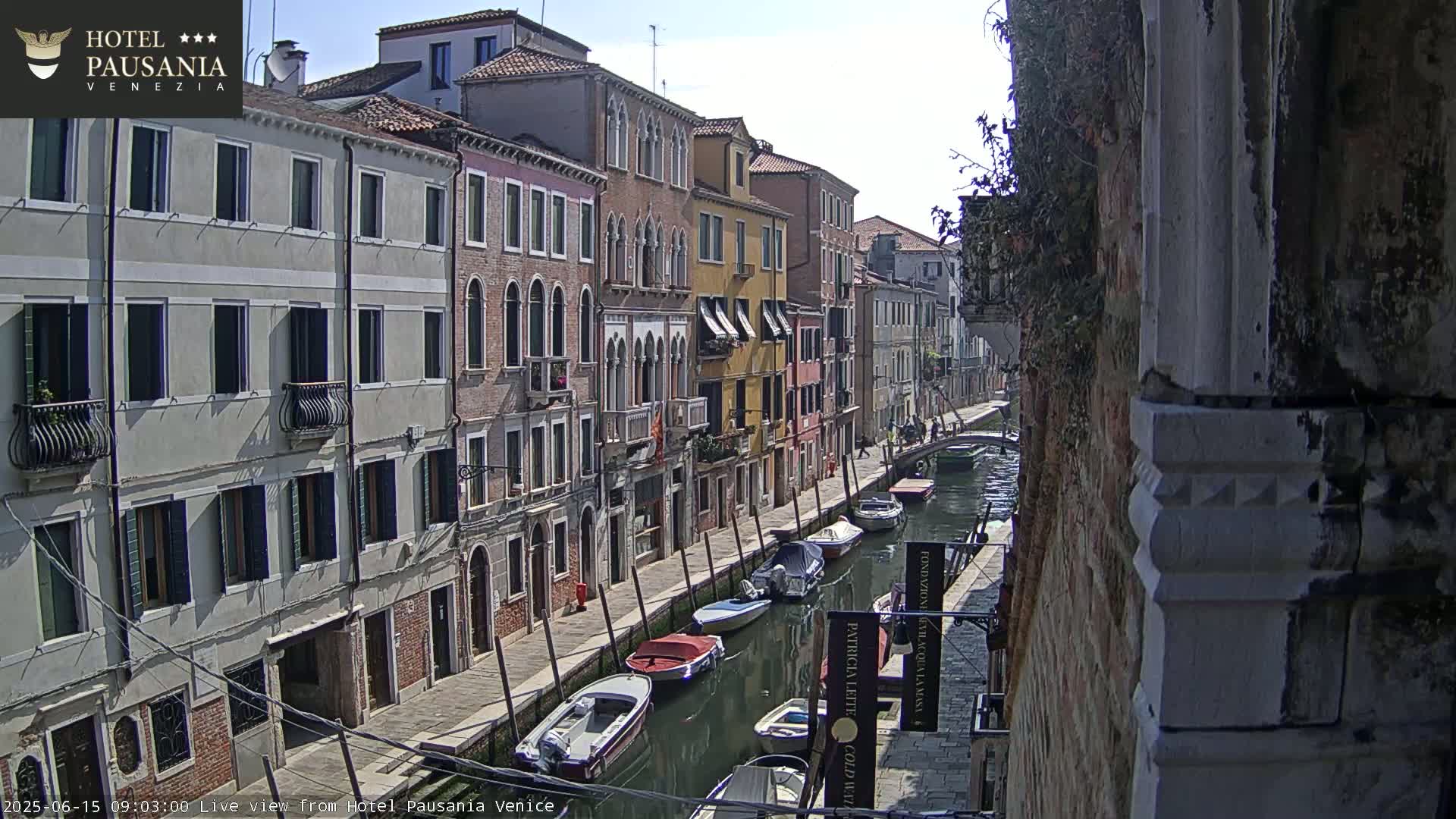 A sunny day in Venice shows several boats moored along a canal beside buildings lining the waterway.