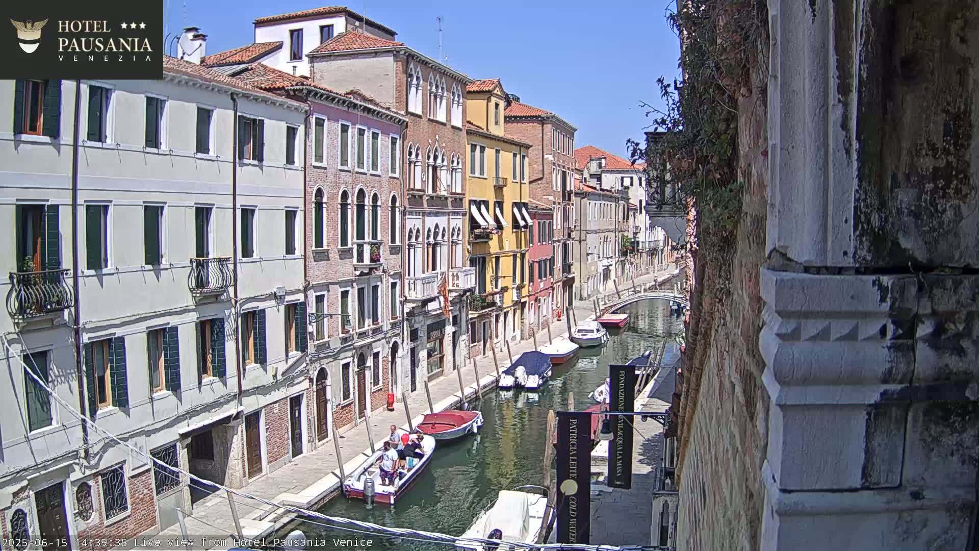 A sunny day in Venice shows several boats on a canal lined with colorful buildings.