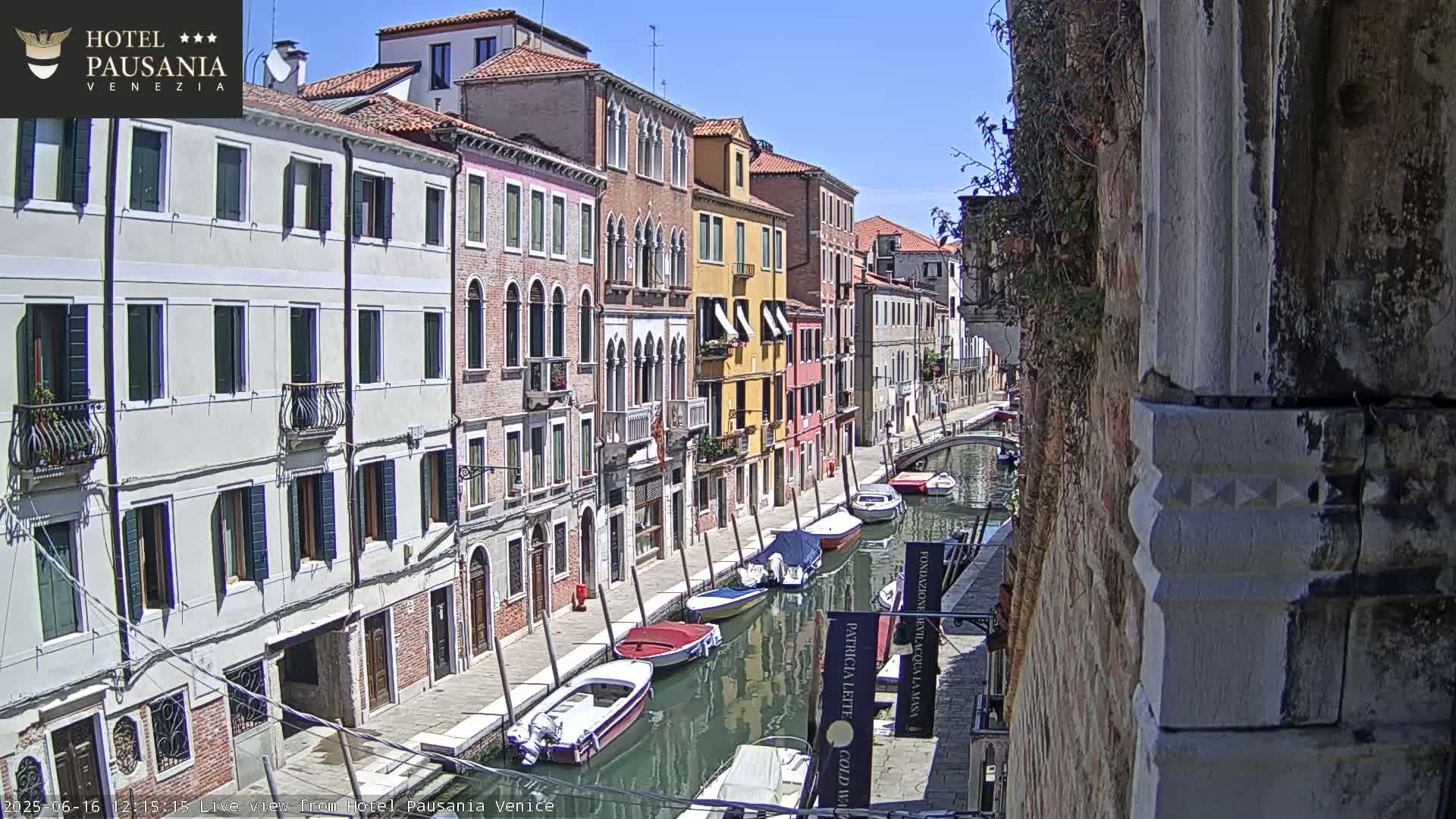 A sunny day in Venice shows several colorful buildings lining a canal with various boats moored along its edge.