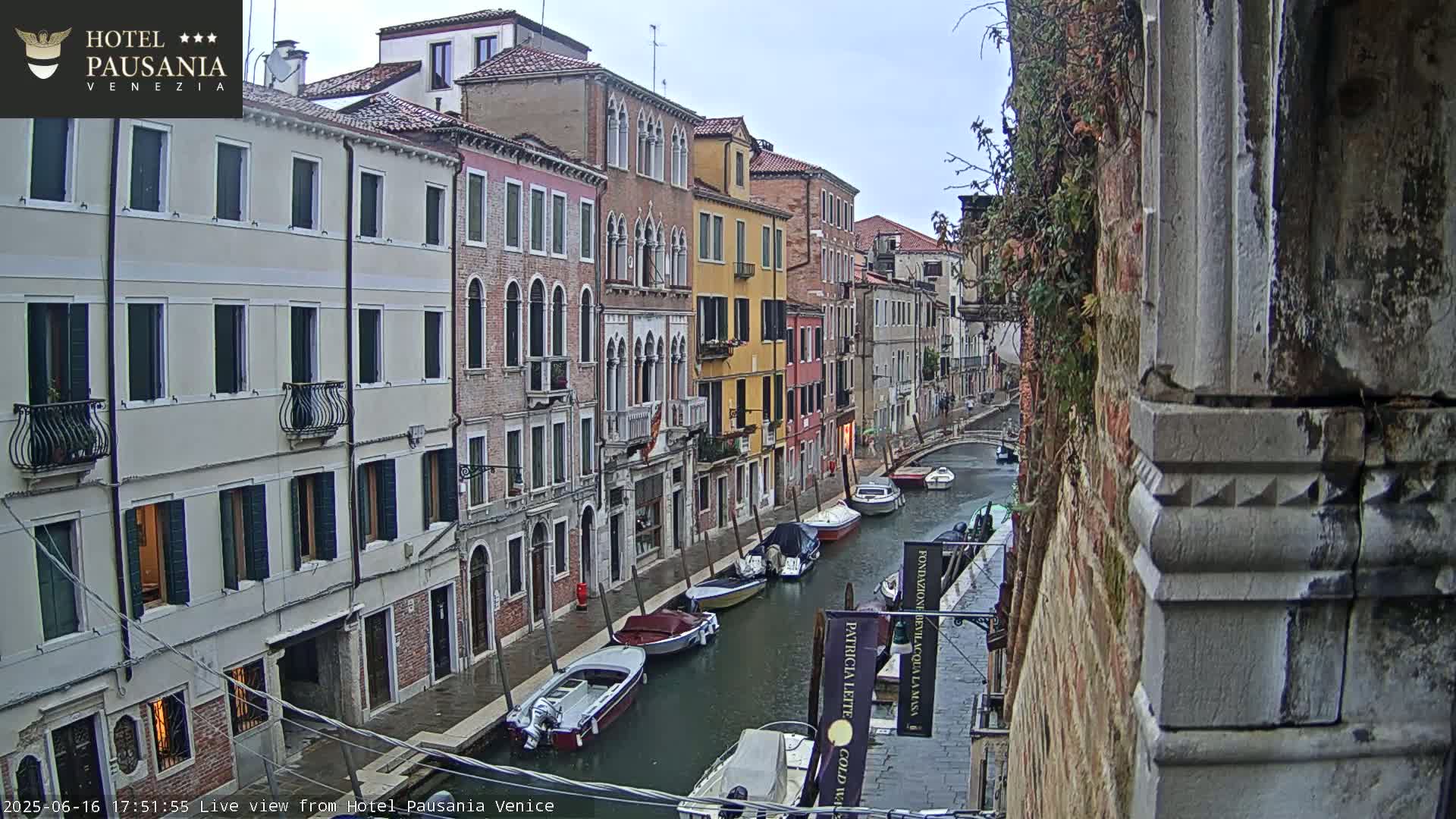 A narrow canal in Venice, Italy, is lined with colorful buildings under an overcast sky; several boats are moored along the waterway.