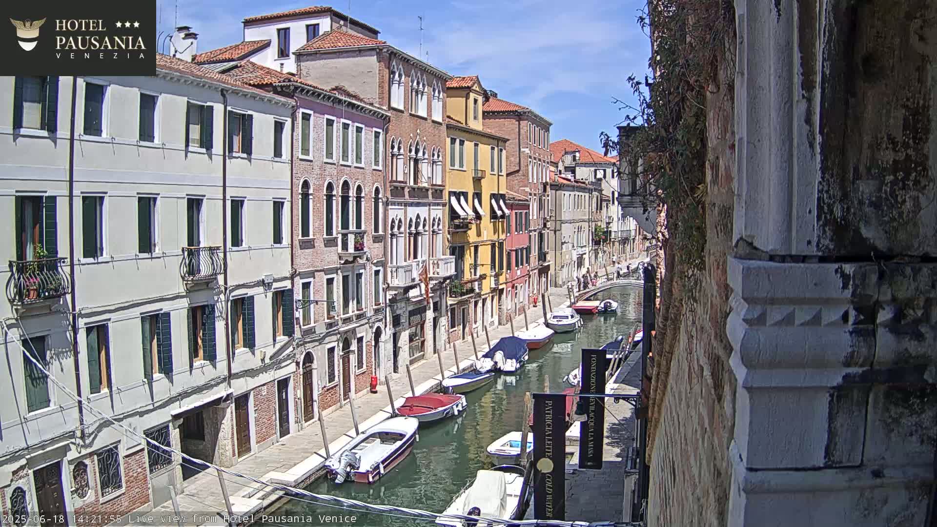 A sunny day in Venice shows several colorful buildings lining a canal filled with motorboats.