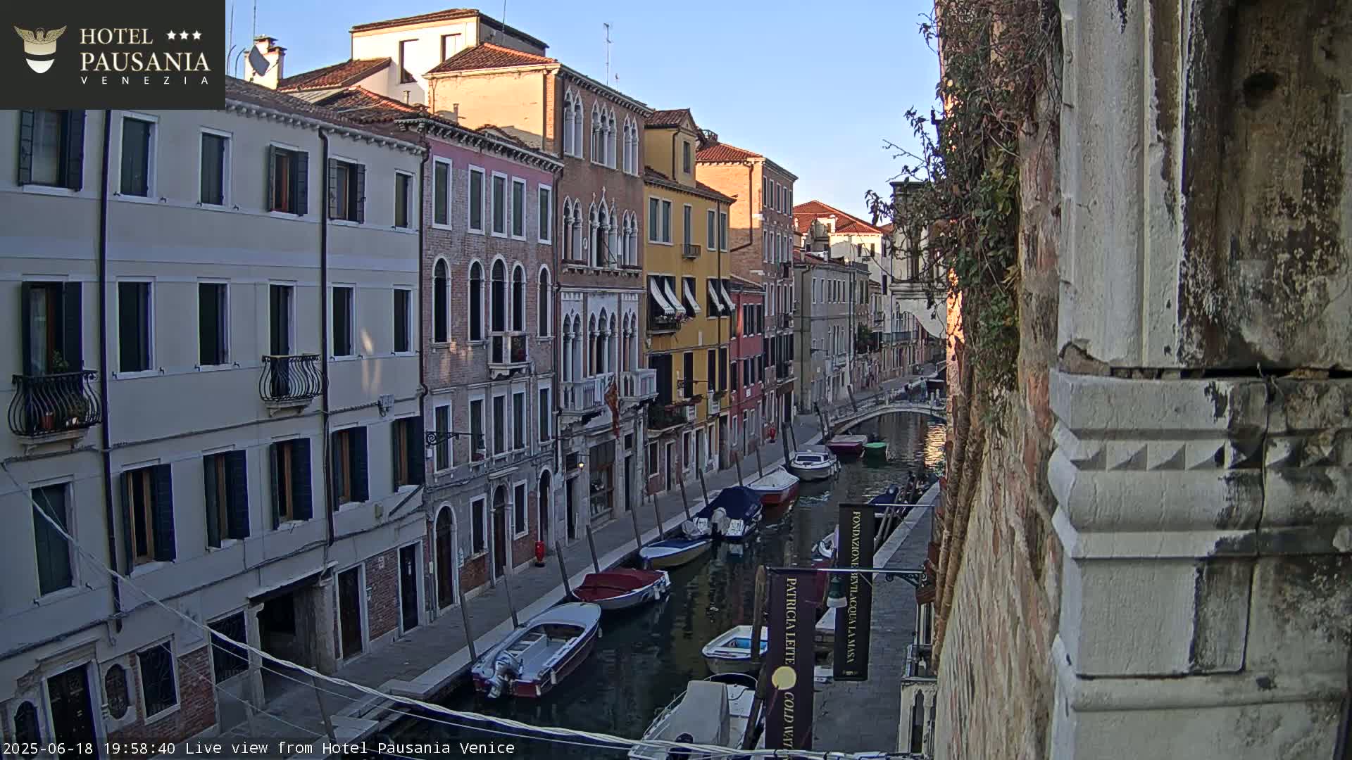 A narrow Venetian canal at sunset, lined with colorful buildings and several moored boats.