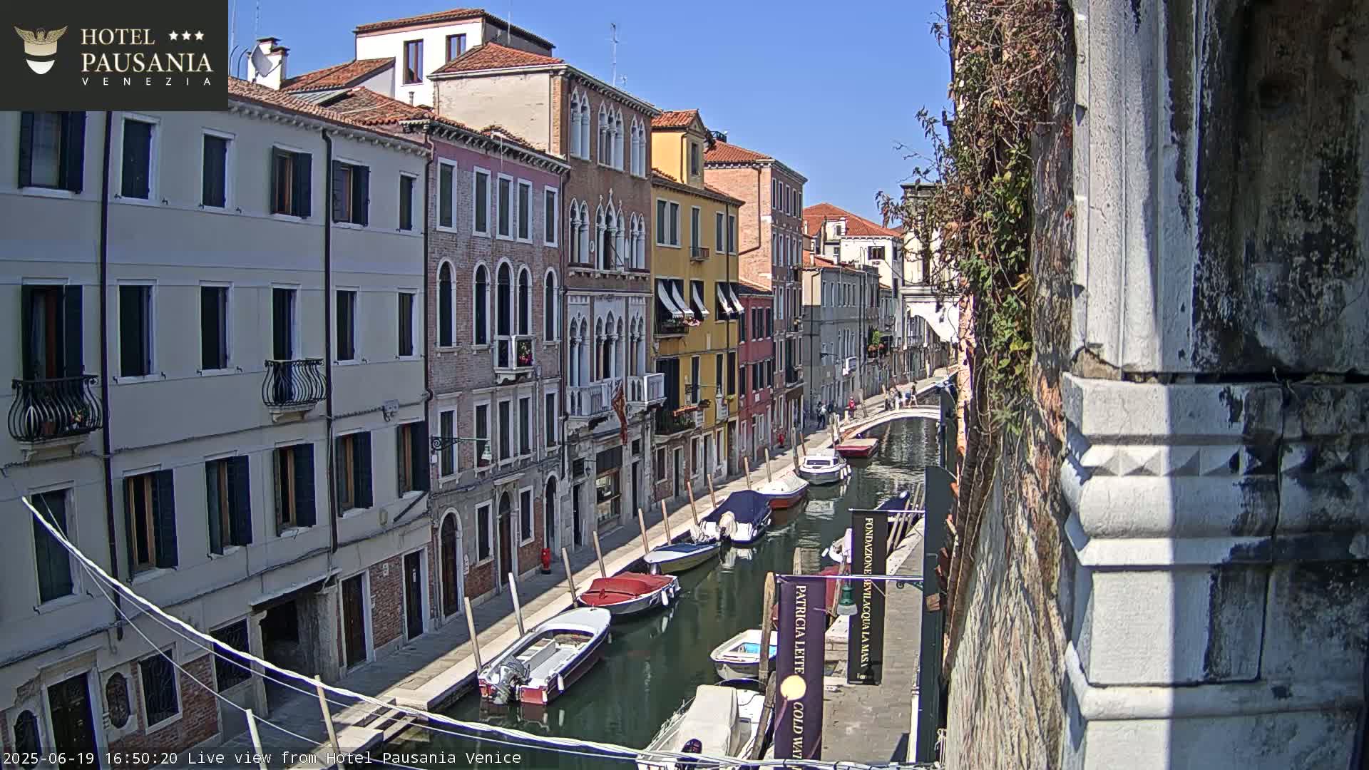 A sunny day in Venice shows several boats moored along a canal lined with colorful buildings.