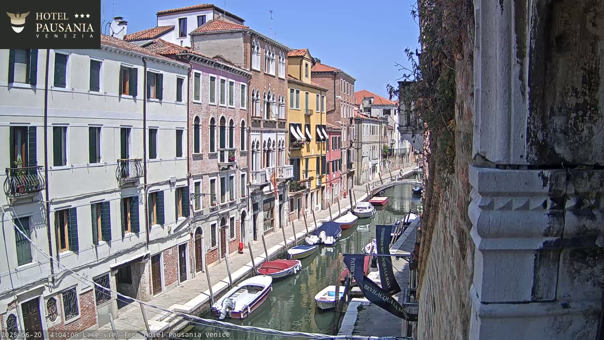 A sunny day in Venice shows a canal lined with colorful buildings and several small boats moored along its edge.