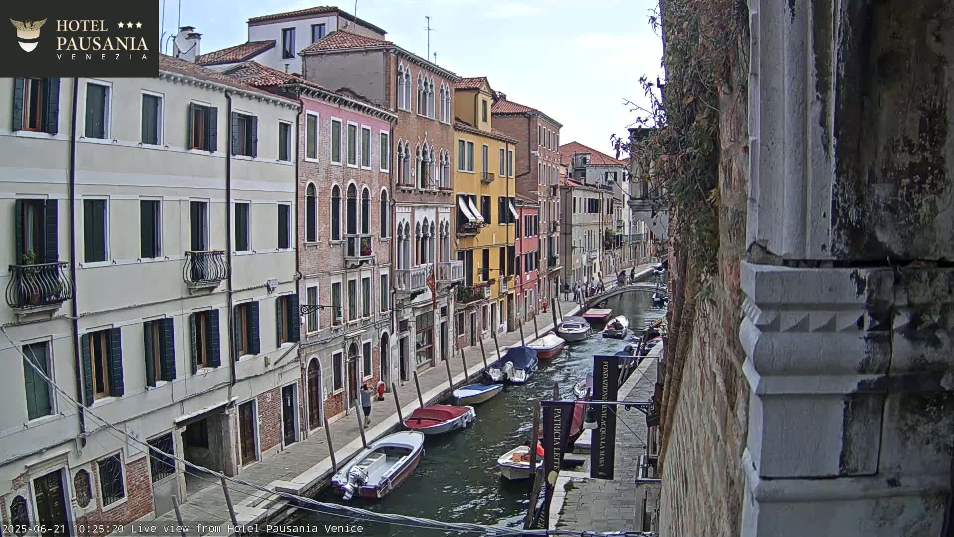 A canal in Venice, under a partly cloudy sky, is lined with colorful buildings and several moored boats.
