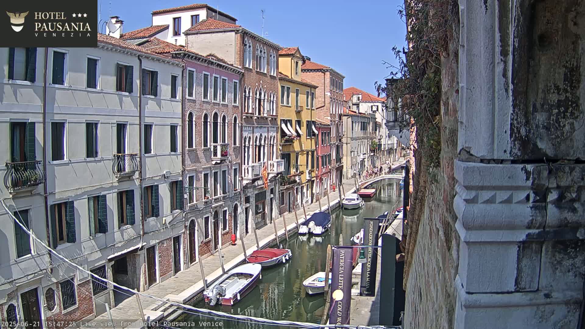 A sunny day in Venice shows several boats moored along a canal lined with colorful buildings.