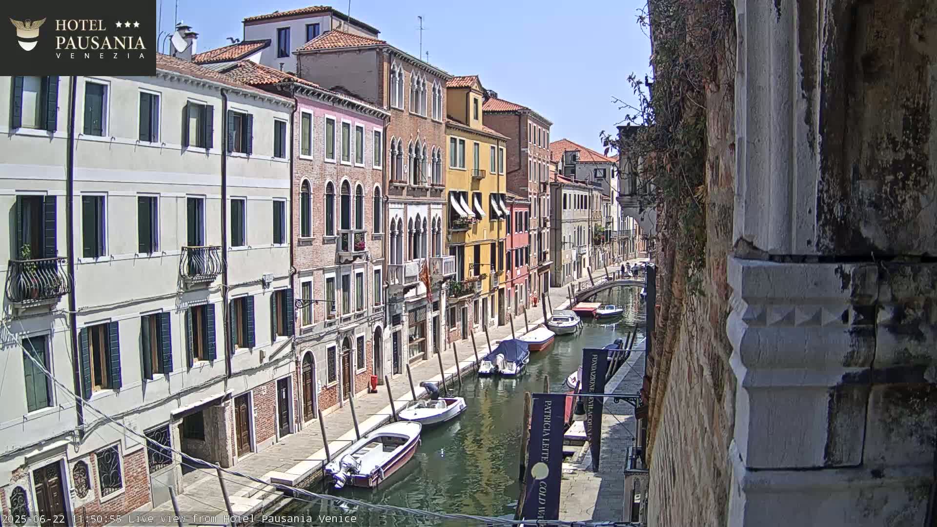 A sunny day in Venice shows several boats moored along a canal lined with colorful buildings.