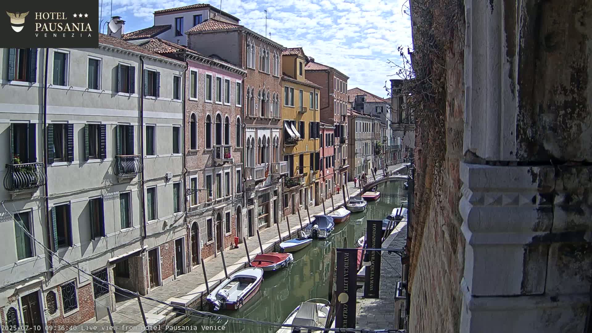 A sunny day in Venice shows several boats moored along a narrow canal beside colorful buildings.