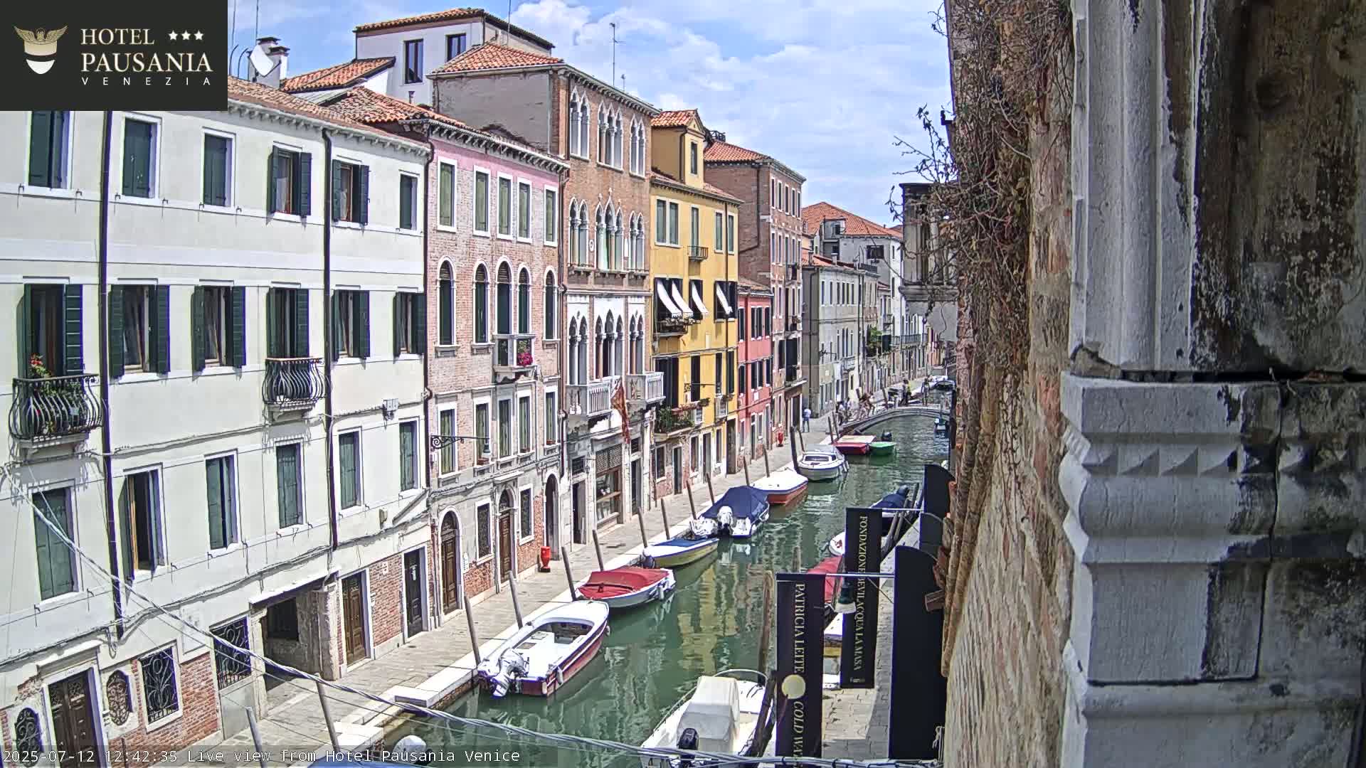 A sunny day in Venice shows several boats moored along a narrow canal beside colorful buildings.