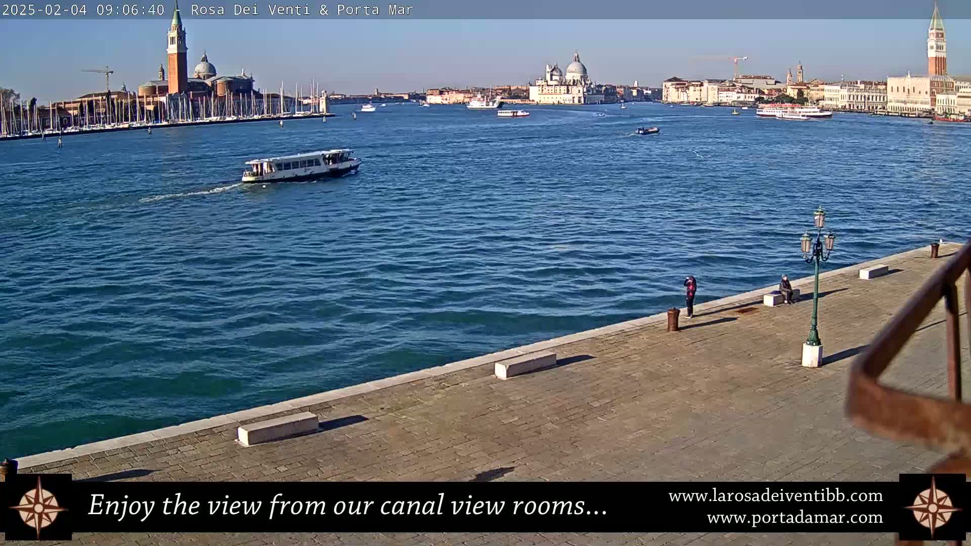 A sunny day reveals a Venetian canal scene with a boat, several people on a stone embankment, and a distant view of buildings including a prominent church dome and bell tower.