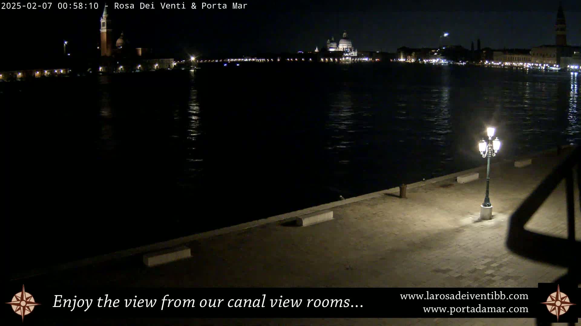 A nighttime view across a calm canal shows a city skyline with lights and a prominent domed building.