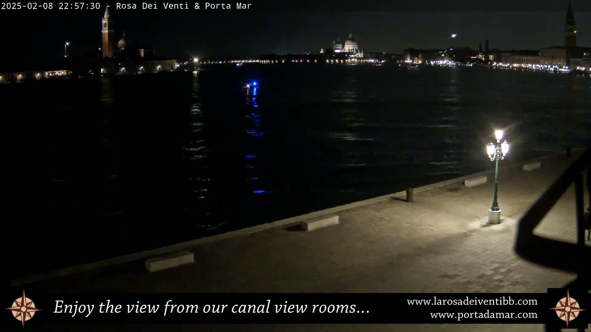 A nighttime view of a canal in Venice, Italy, shows calm water reflecting city lights and buildings across the waterway.