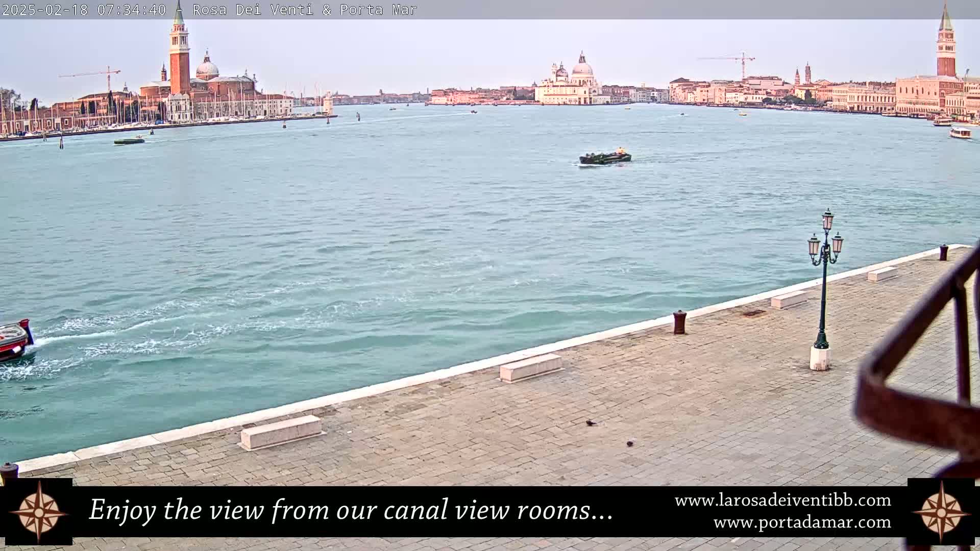 A calm canal in Venice, Italy, with a view of several buildings, including a large church, under a mostly clear sky.