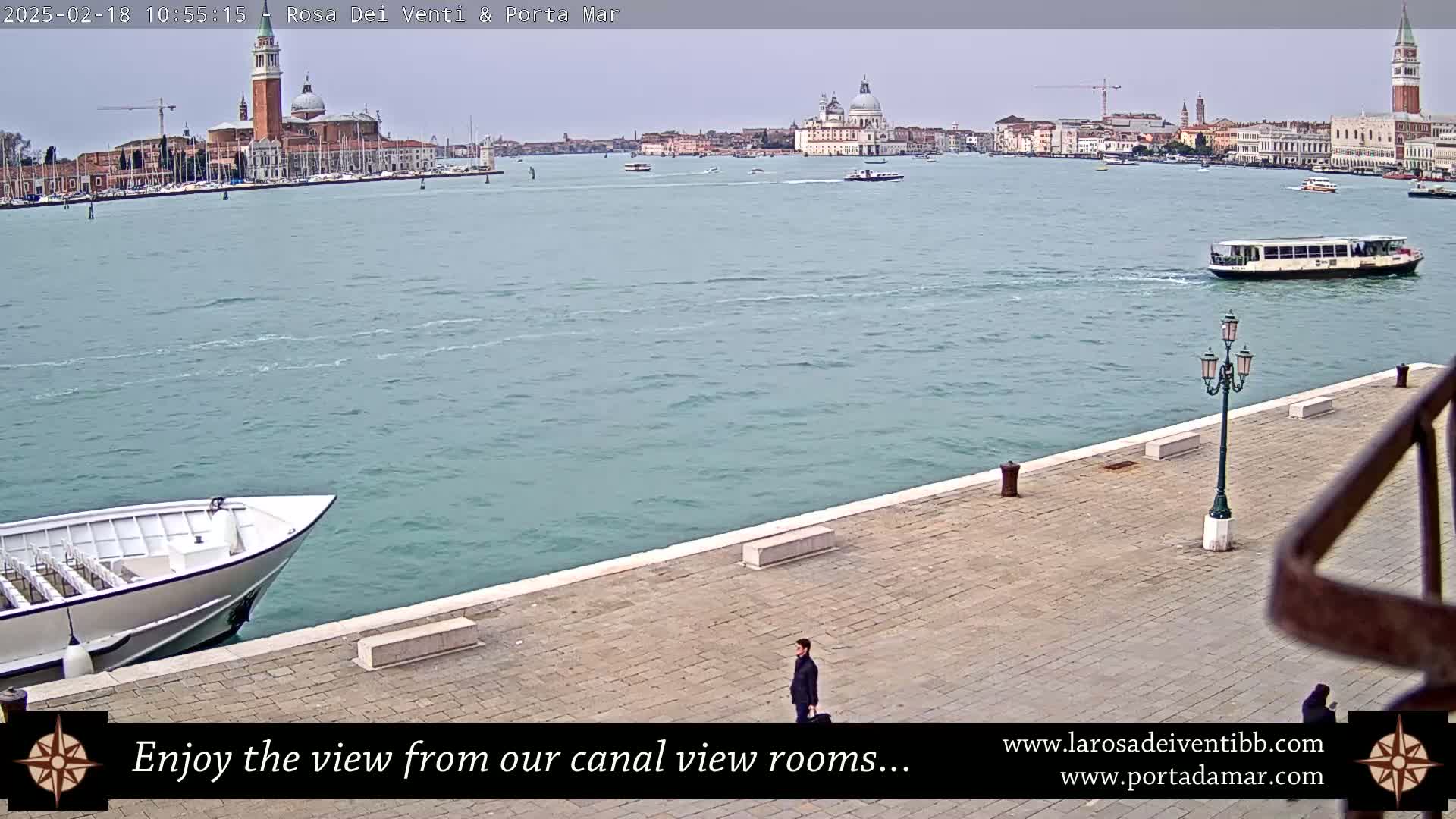 A waterfront view of a canal in Venice, Italy, on an overcast day shows boats on the water and buildings in the distance.