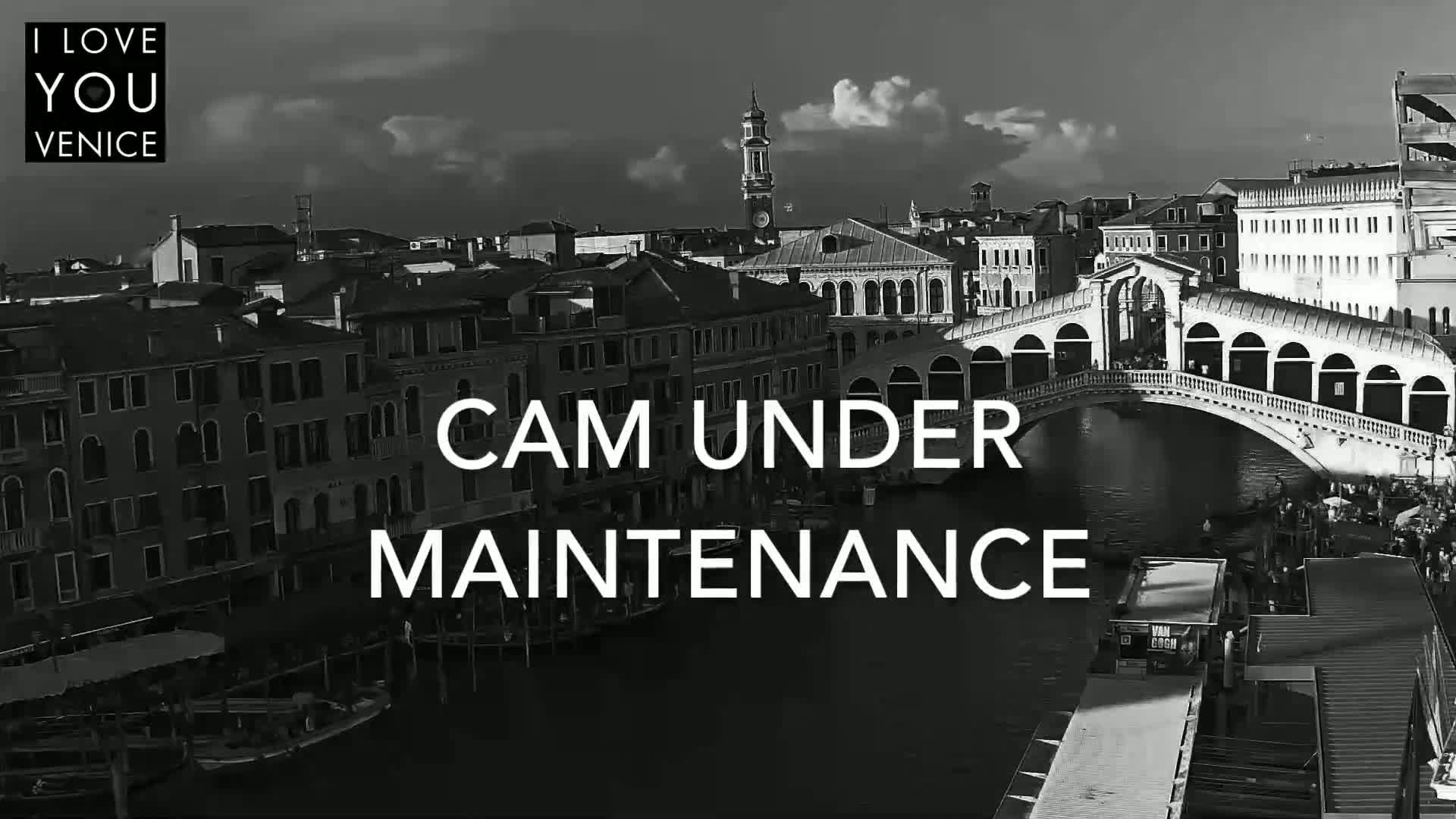 A black and white view of a bridge over a canal in Venice, under a partly cloudy sky.