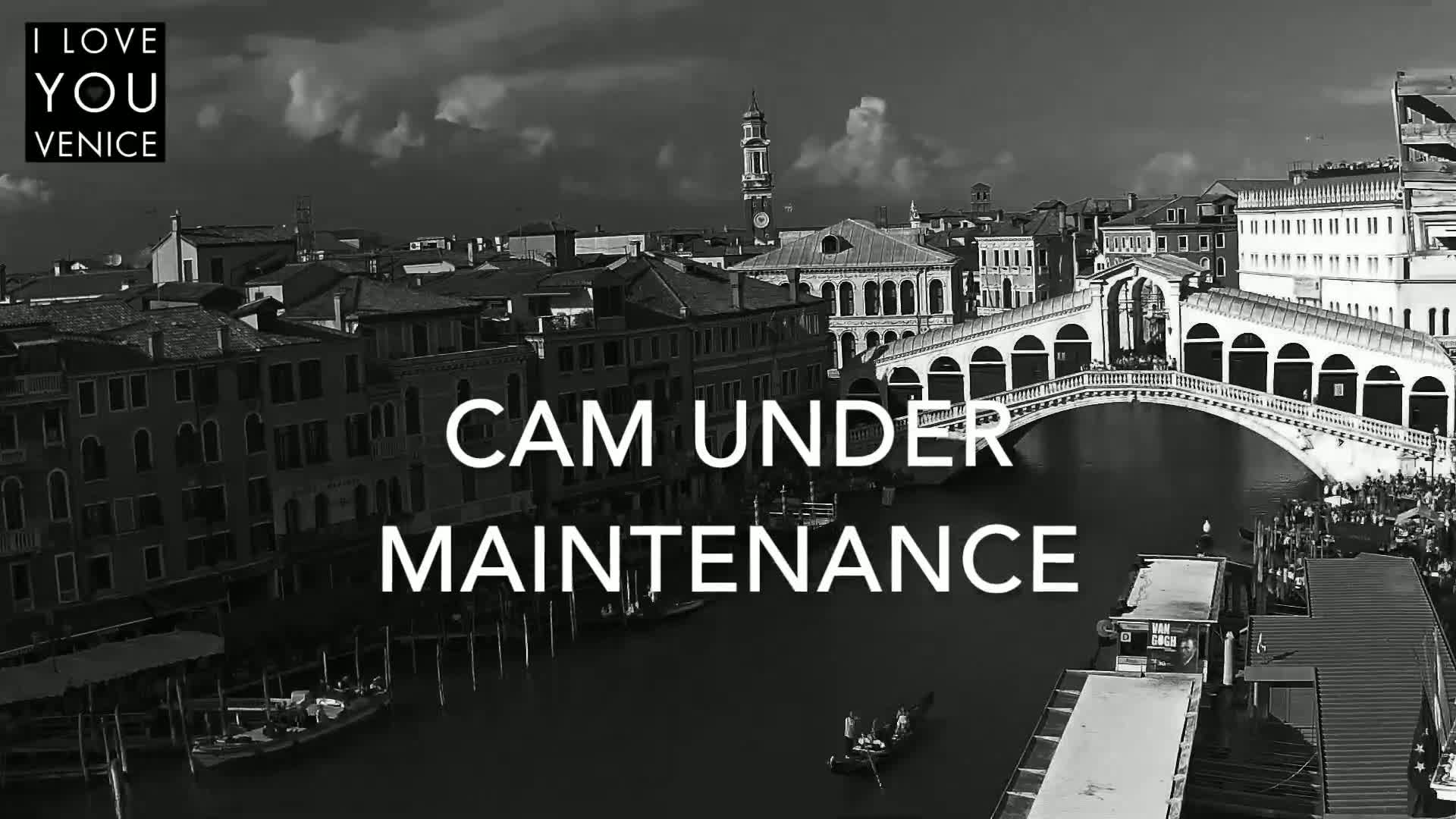 A black and white, high-angle view shows a gondola on a canal under a bridge in Venice, with overcast skies.