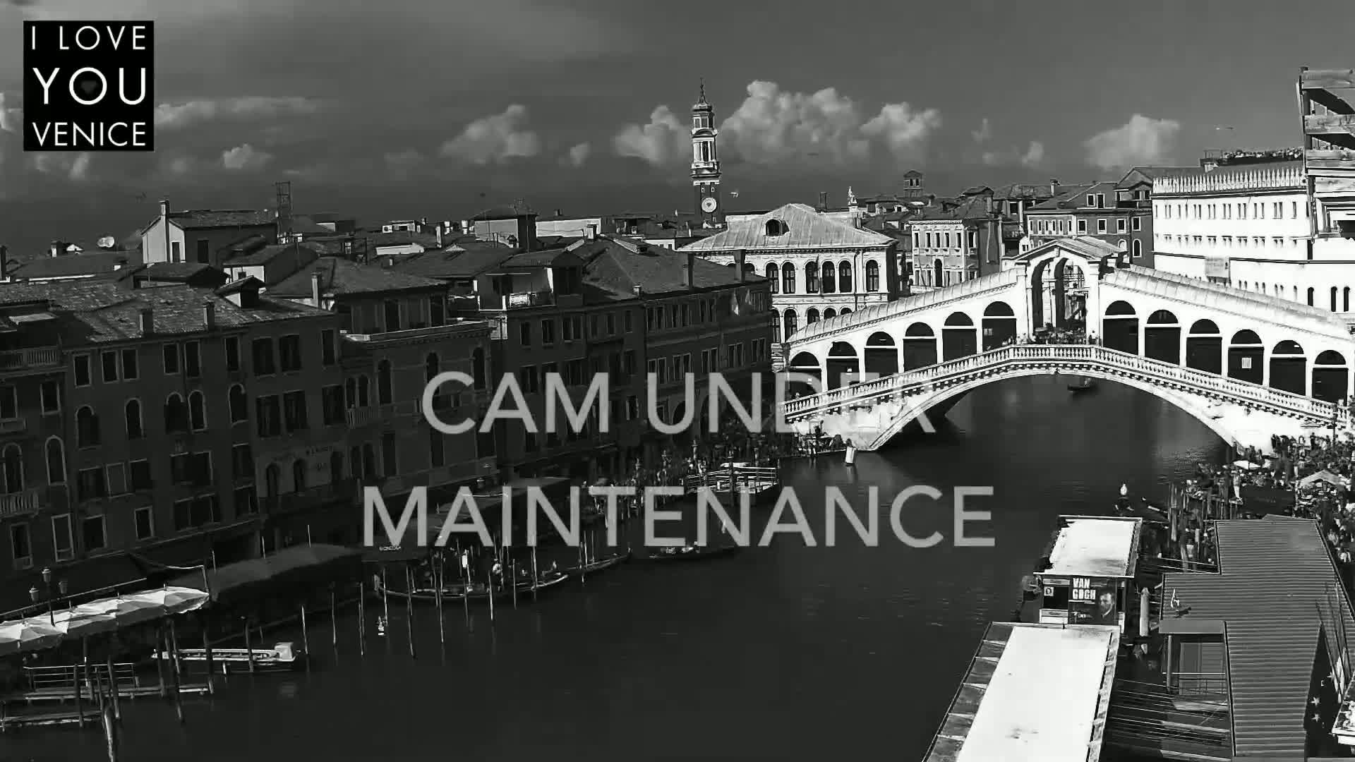 A black and white, high-angle view shows a bridge over a canal in Venice under a partly cloudy sky.