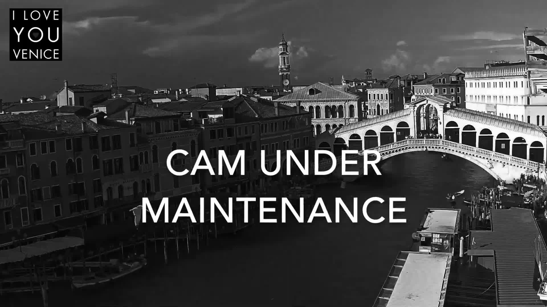 A black and white image captures an overcast day in Venice, featuring the Rialto Bridge spanning a busy canal lined with historic buildings and boats.