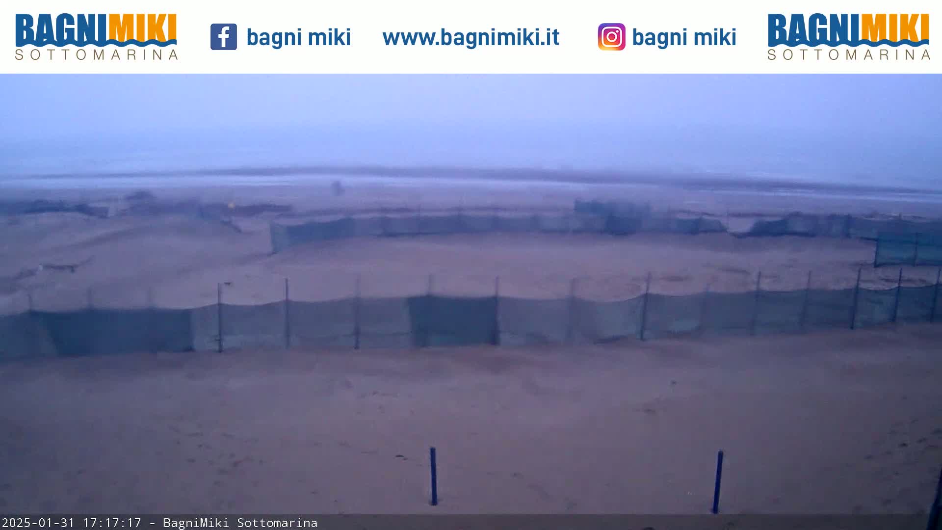 A sandy beach with several enclosed areas surrounded by netting is visible under an overcast sky.
