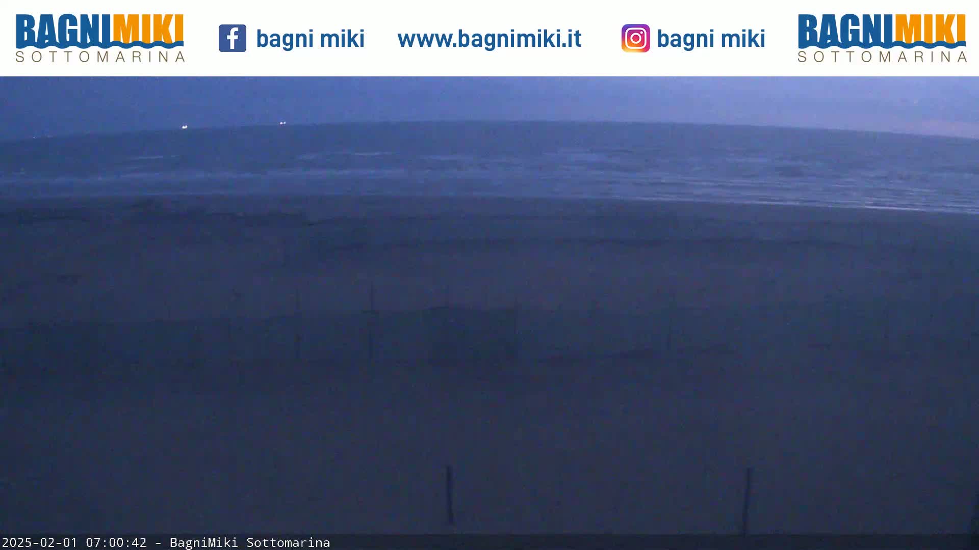A dark, sandy beach meets a choppy sea under a twilight sky.