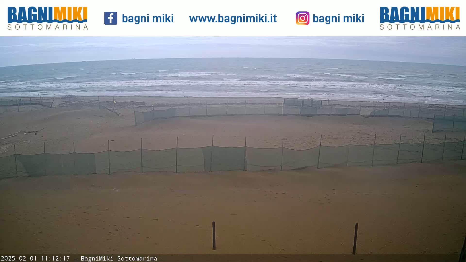 A sandy beach with several sections enclosed by netting is visible, overlooking a somewhat choppy sea under an overcast sky.
