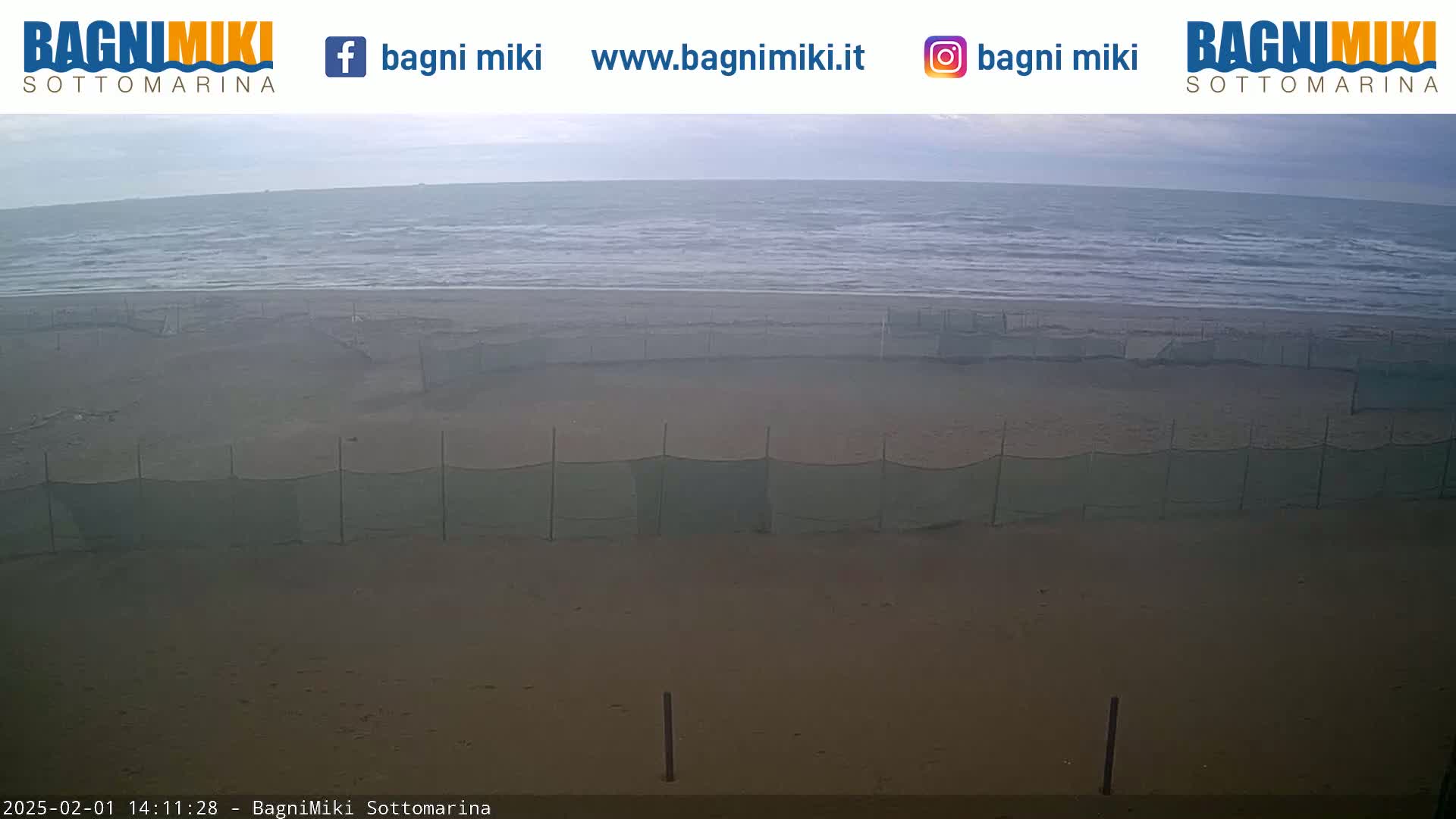 A sandy beach with a wavy ocean under an overcast sky is sectioned off by several mesh fences.