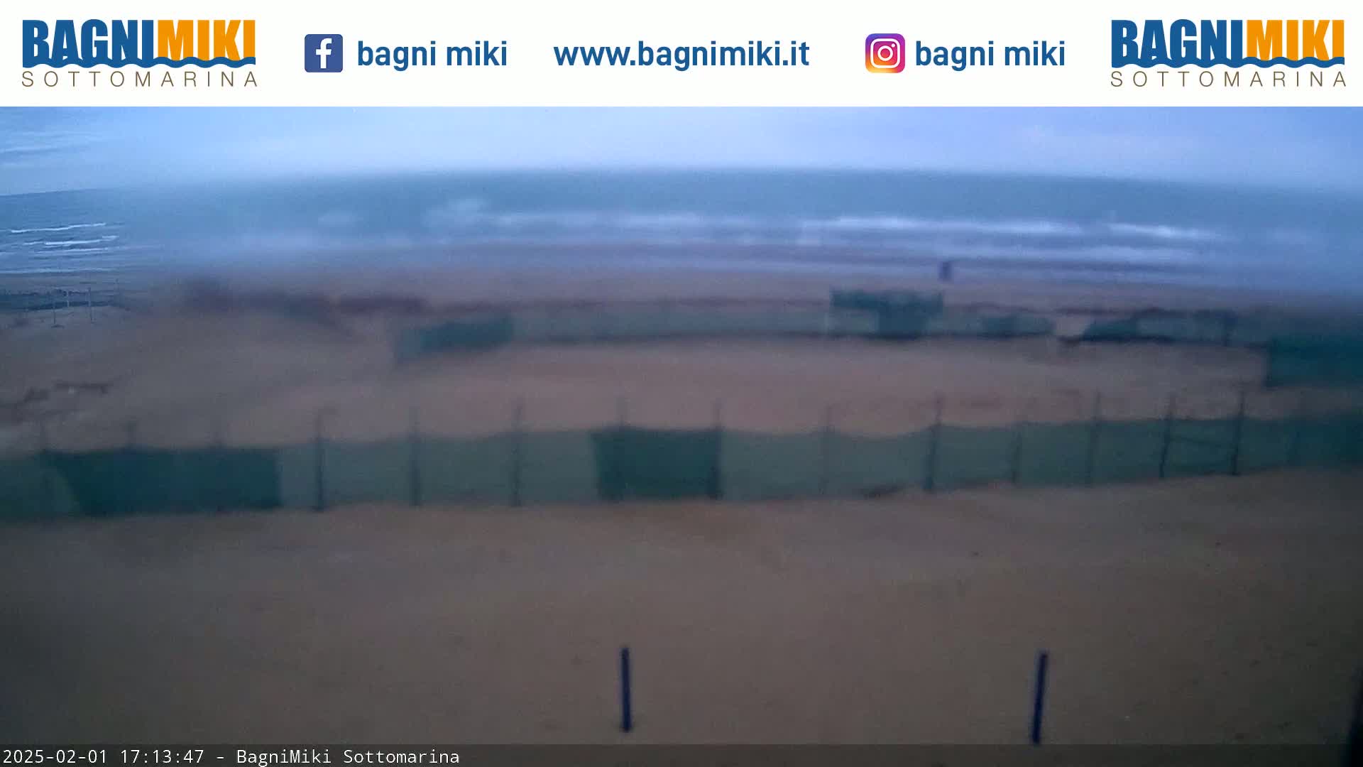 A sandy beach with a fence is visible, with a somewhat overcast sky and a choppy ocean in the background.