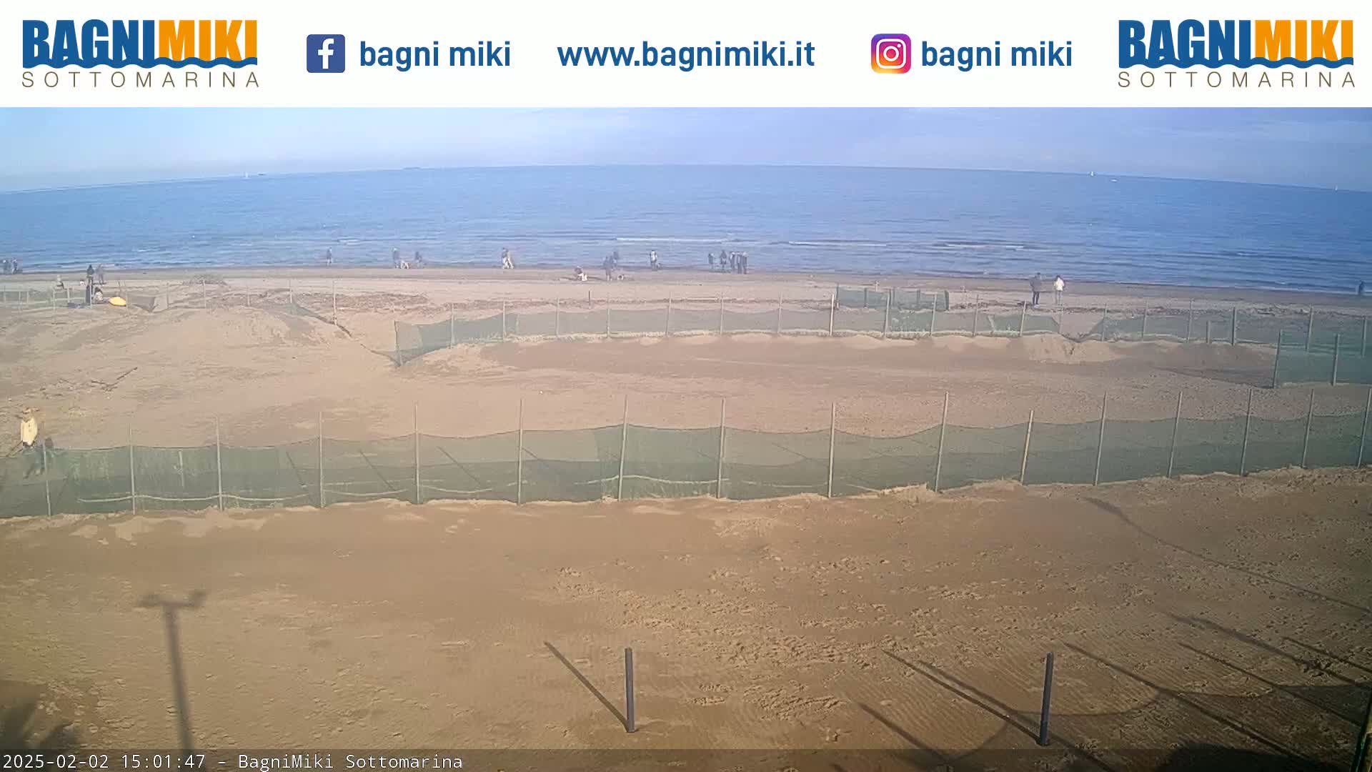 A sandy beach with several fenced-off sections is visible, overlooking a calm ocean under a clear sky.