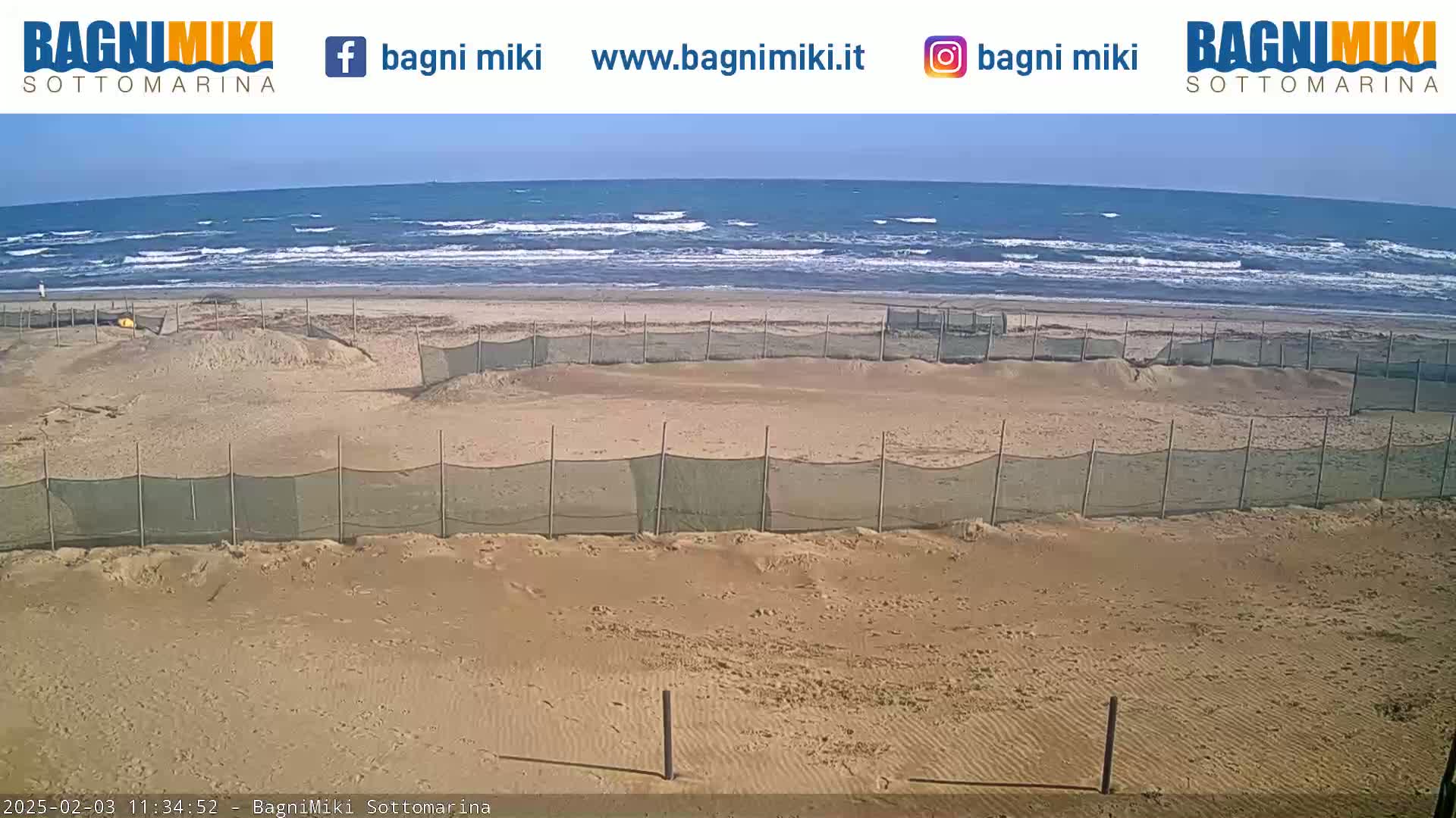 A sandy beach with several enclosed areas protected by netting is visible, overlooking a moderately wavy ocean under a clear sky.