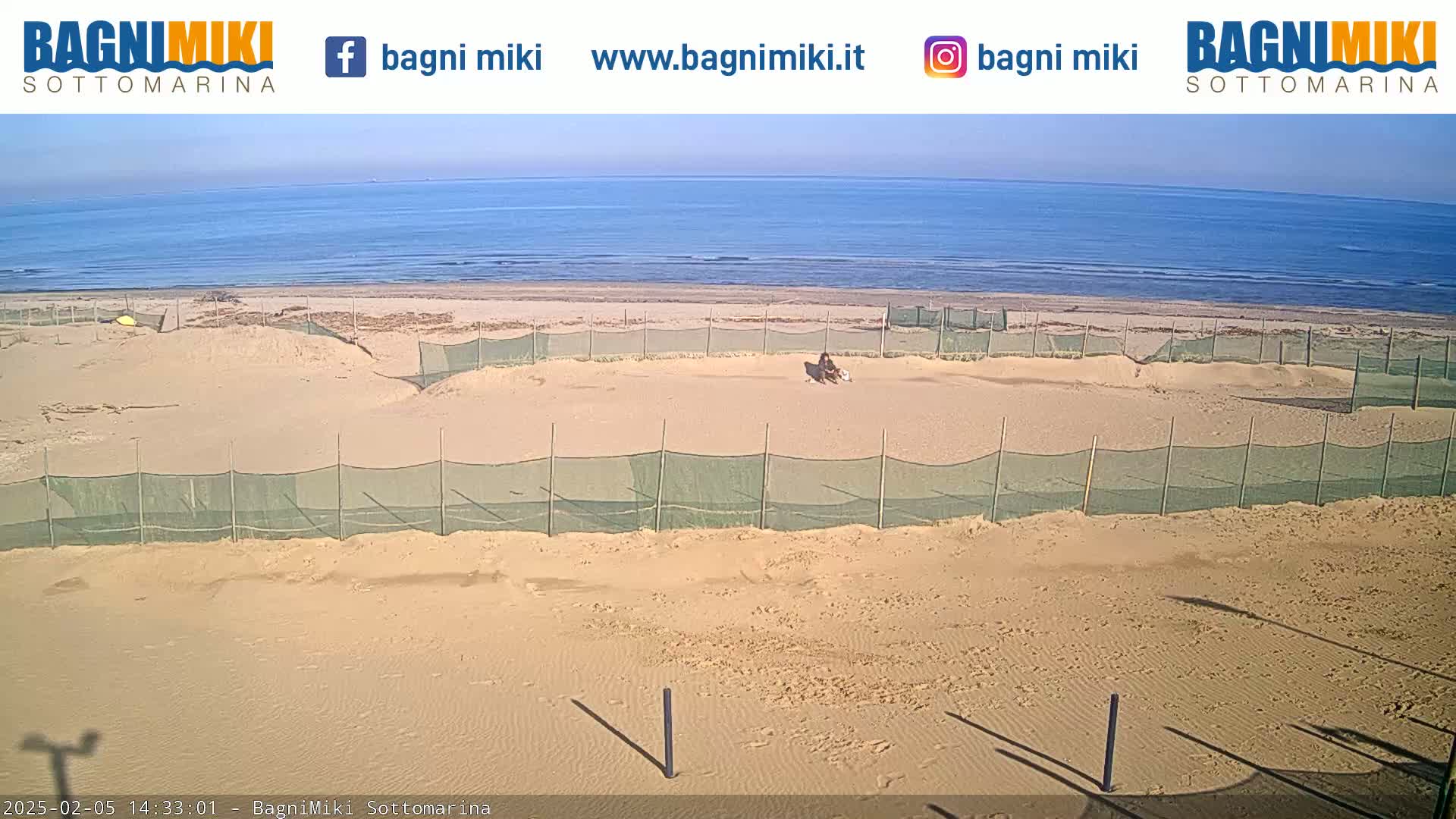 A sandy beach with several enclosed areas protected by netting is visible, overlooking a calm ocean under a mostly clear sky.