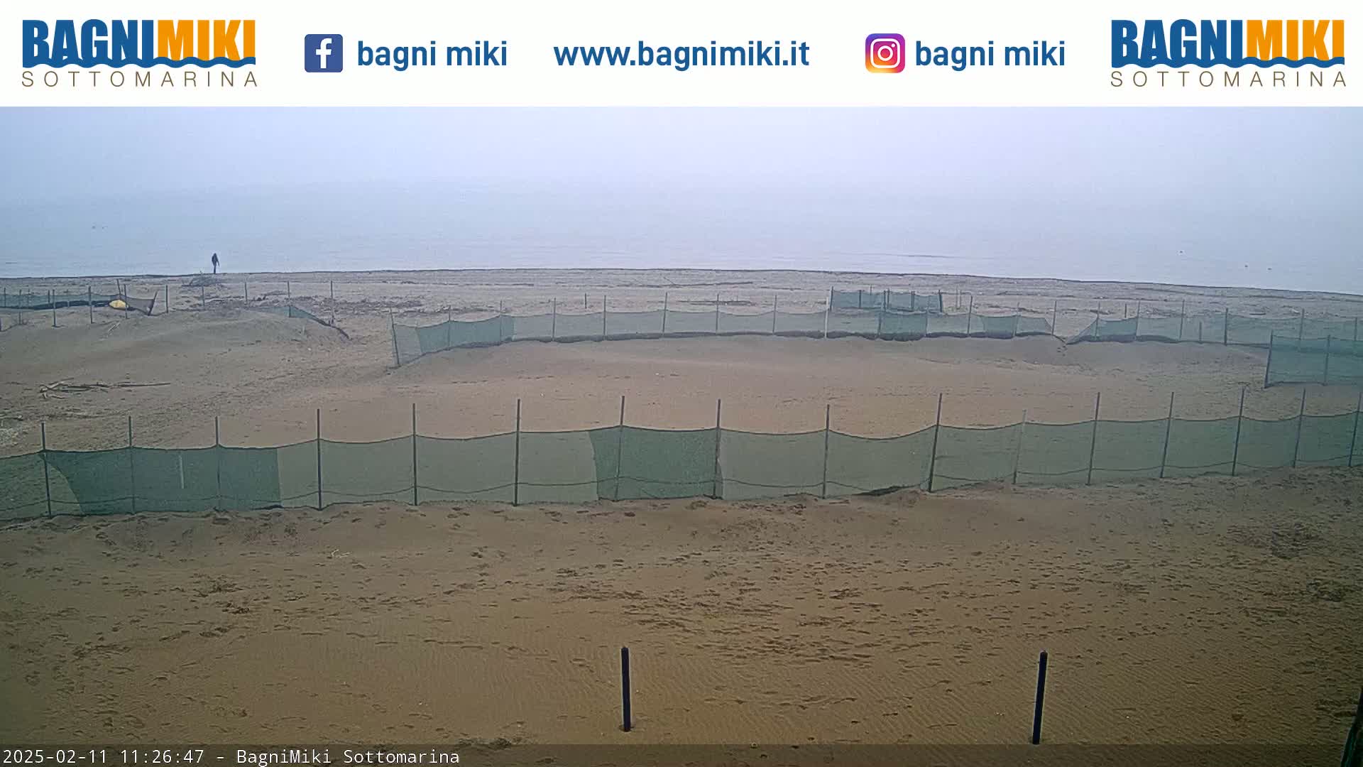 A sandy beach with several sections enclosed by green netting is visible under an overcast sky.